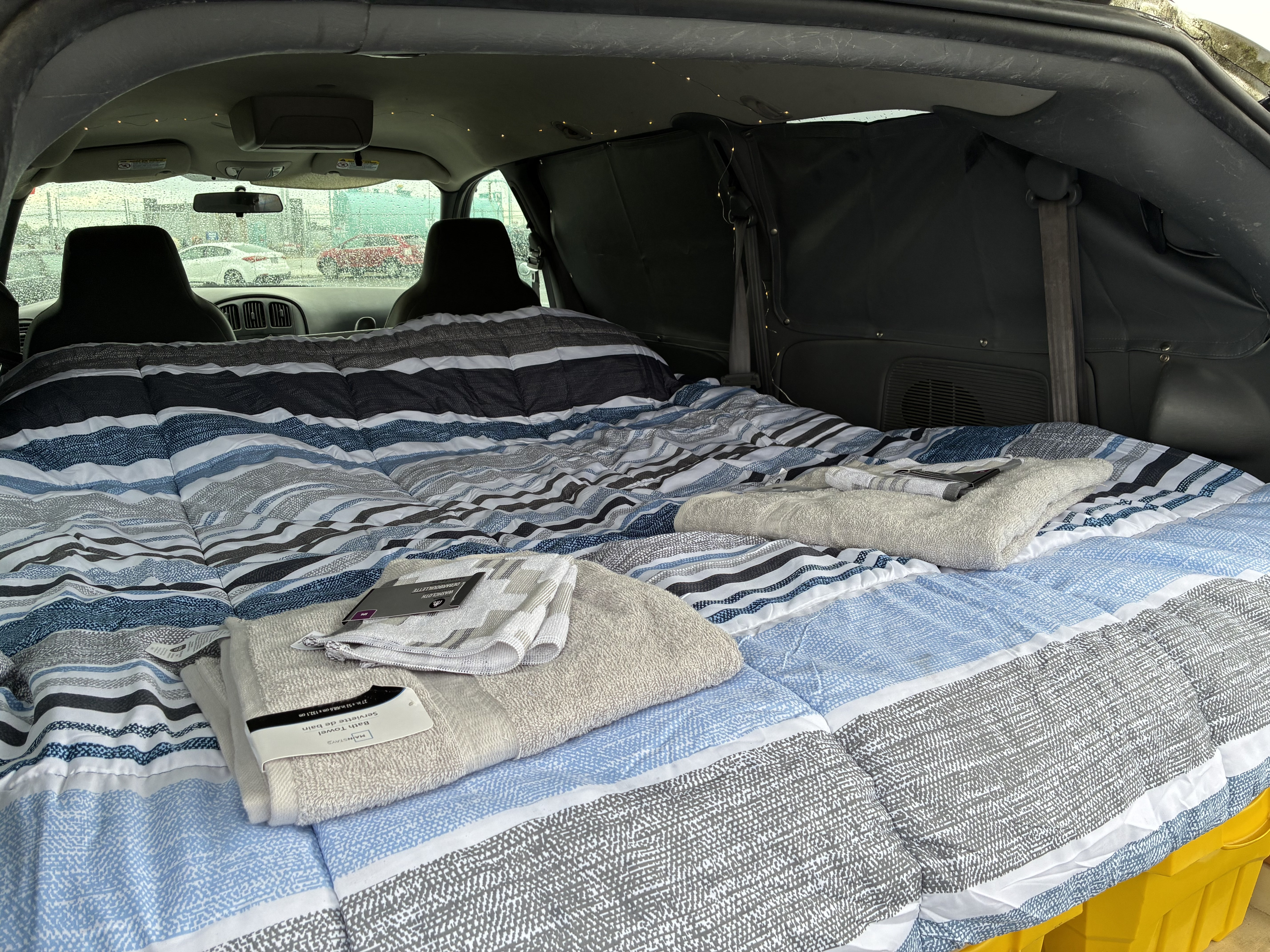 Cozy mobile bedroom in a van, featuring striped bedding and new towels, ideal for an RV rental or car camping trip.. Dodge Grand Caravan 2005
