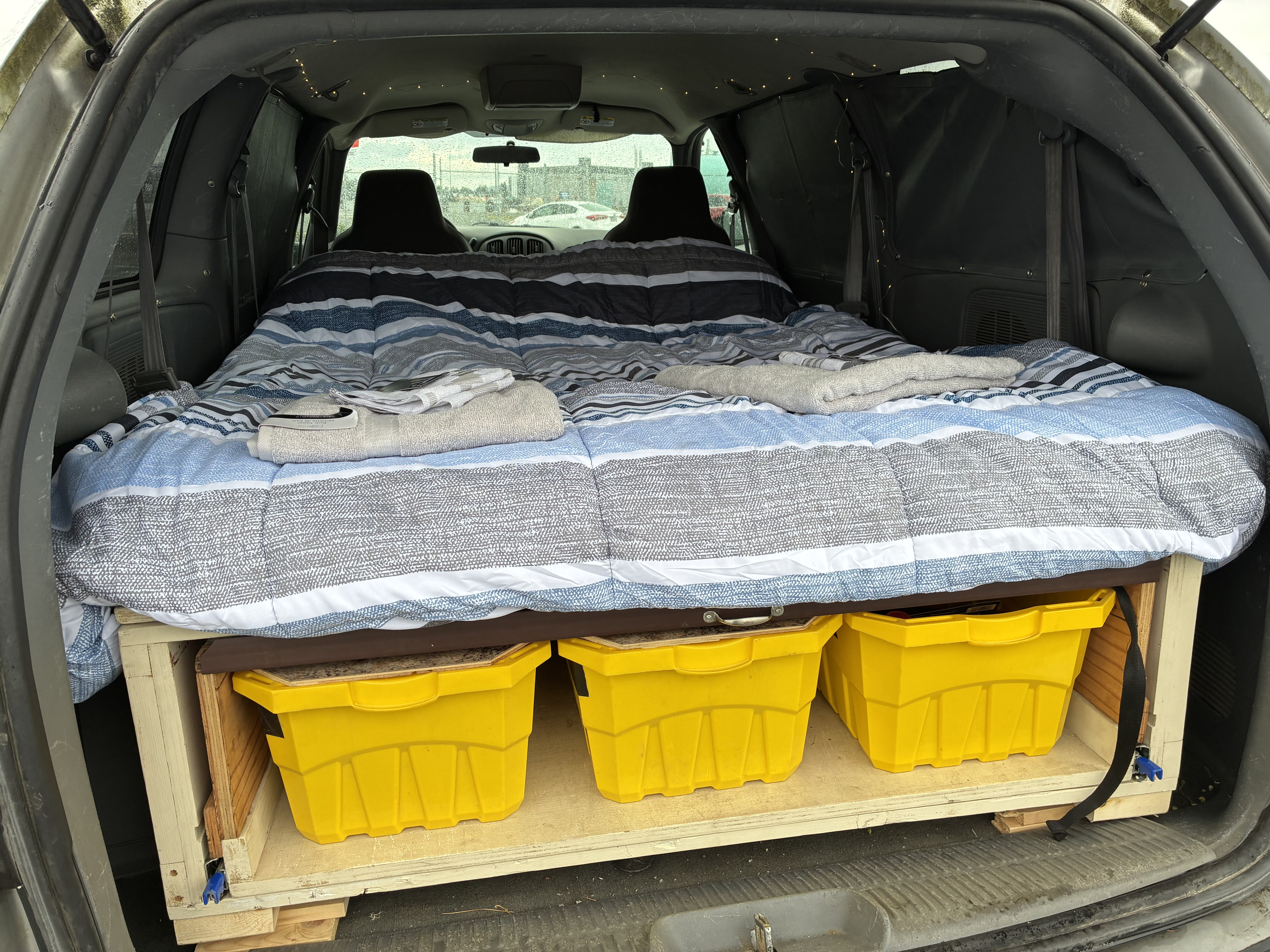 RV rental: Minivan camping setup with striped bed, under-bed storage in yellow bins, side privacy panels, and fairy lights.. Dodge Grand Caravan 2005