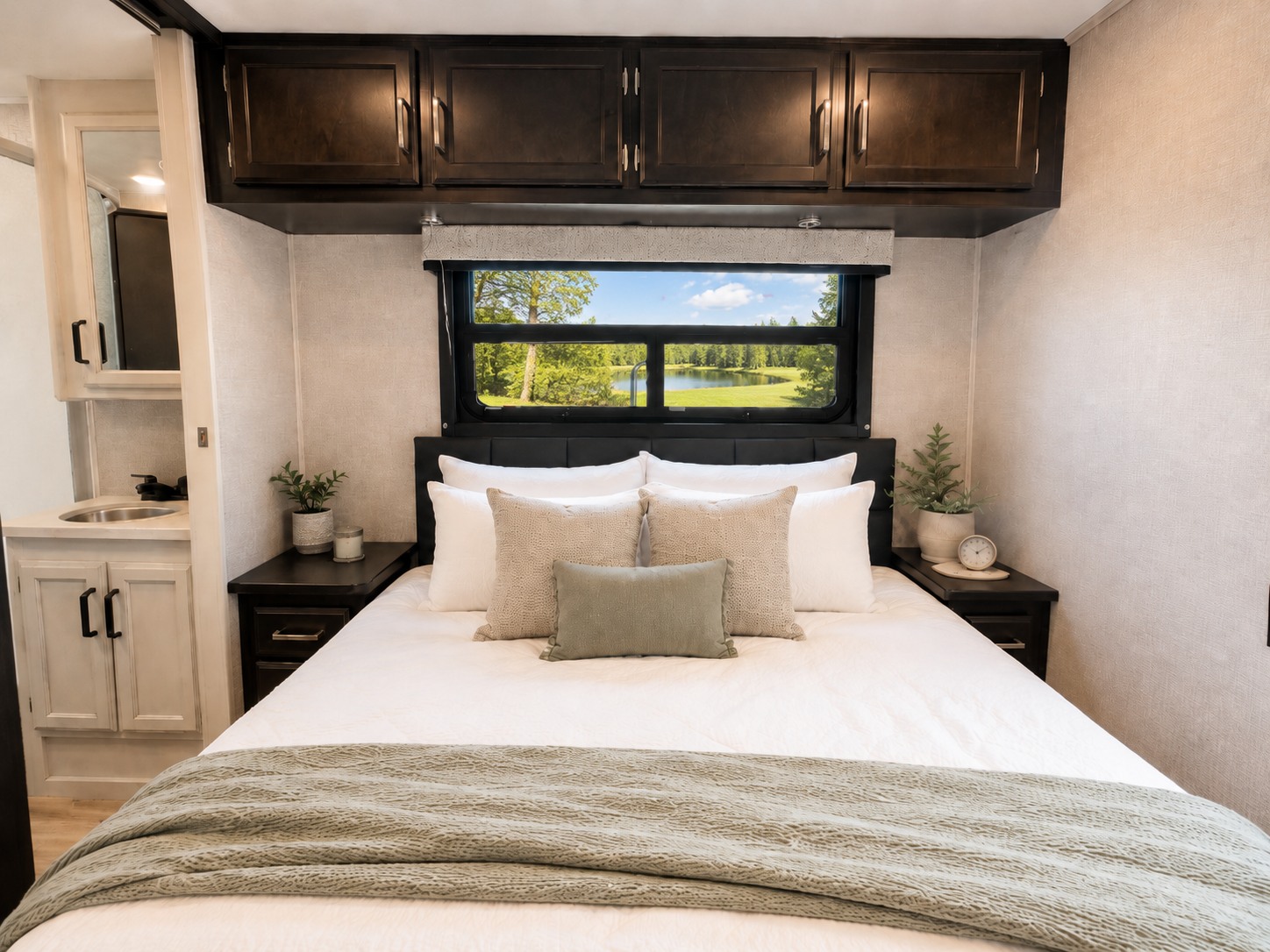 Cozy RV rental bedroom with comfortable bed, scenic window view, and built-in storage. Features a small sink area on the left.. Jayco Redhawk 2024