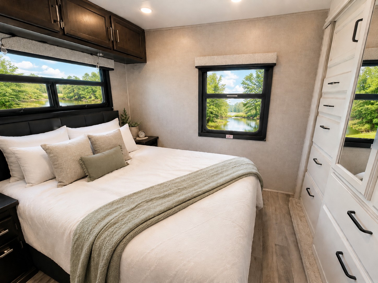 This comfortable RV rental bedroom offers a large bed, storage, and scenic windows overlooking a tranquil lake.. Jayco Redhawk 2024
