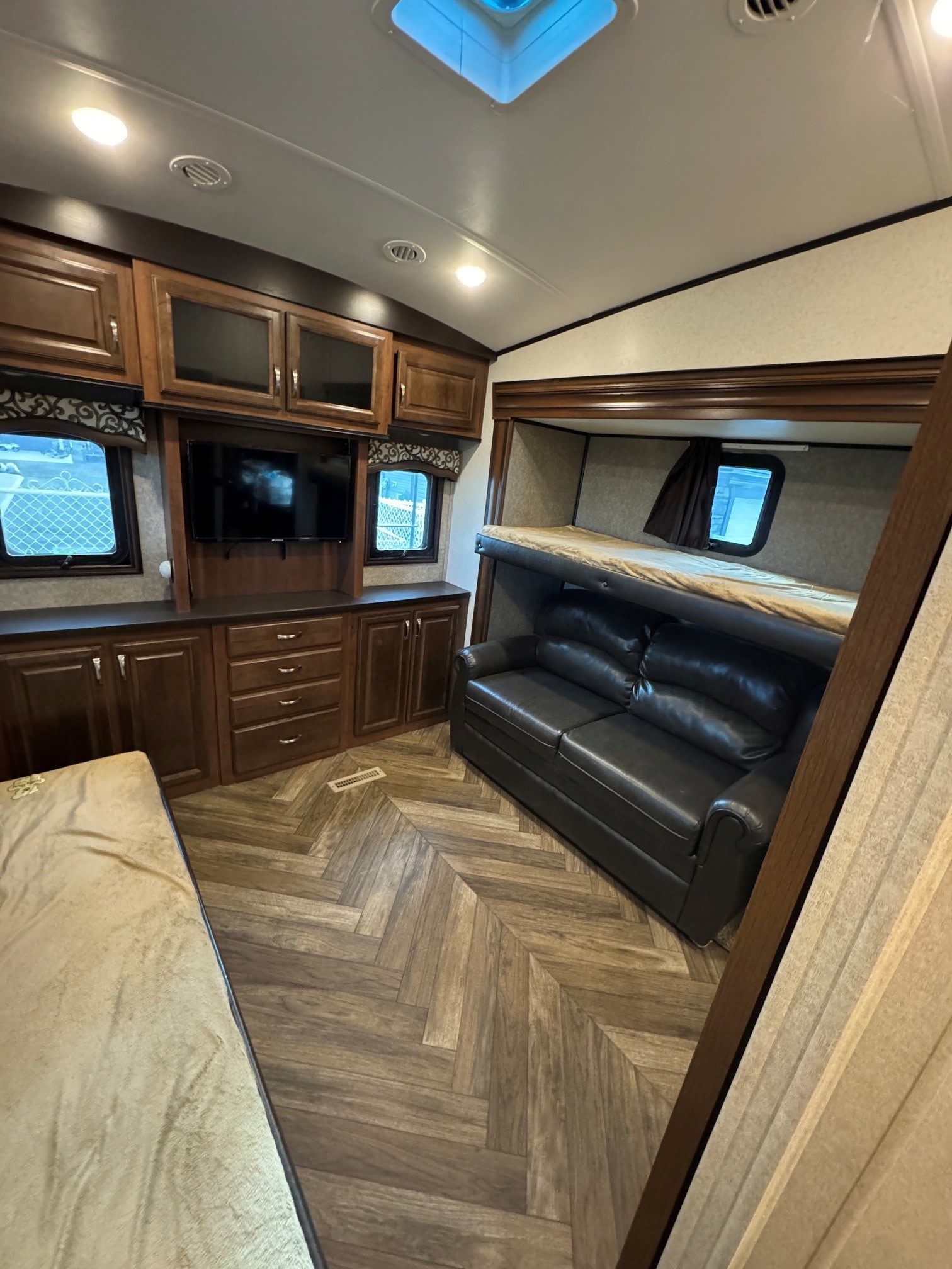 RV rental bunkhouse interior: dark wood cabinets, TV, sofa, and upper bunk. Herringbone floor and cozy lighting.. Jayco North Point 2017