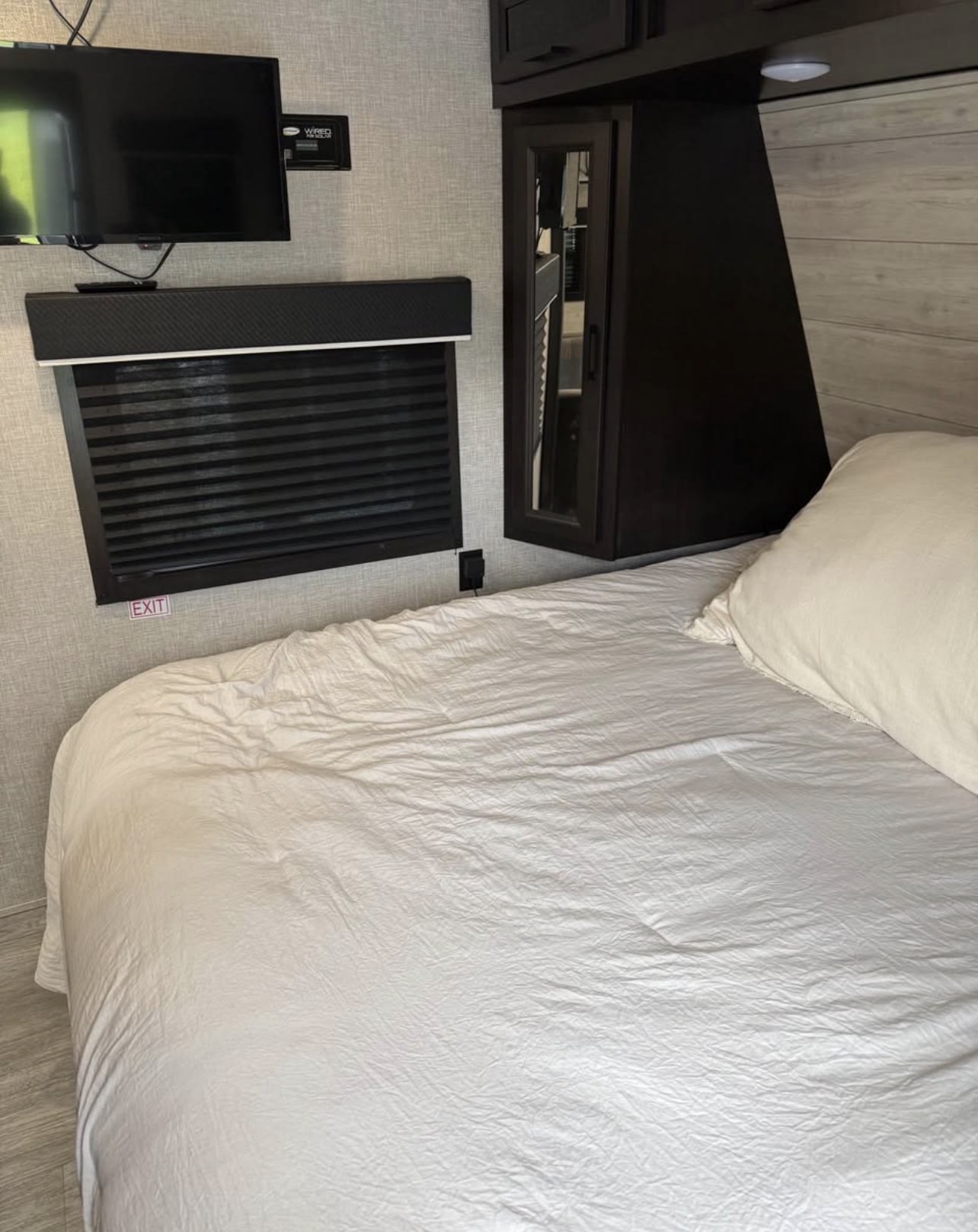RV rental bedroom interior with a white bed, TV, window, and dark wood storage cabinets, offering compact comfort.. Jayco Jay Flight 2022