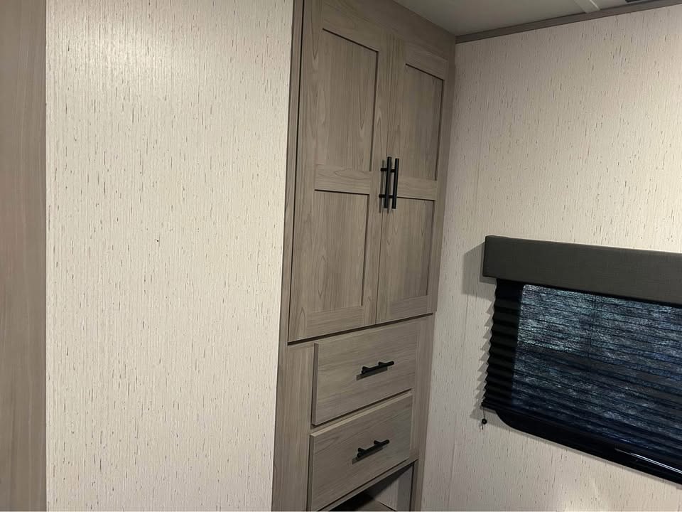**RV rental** interior features light-textured walls, a wooden cabinet with drawers, and a dark pleated window blind, providing compact storage.. Coleman 270TQ 2022