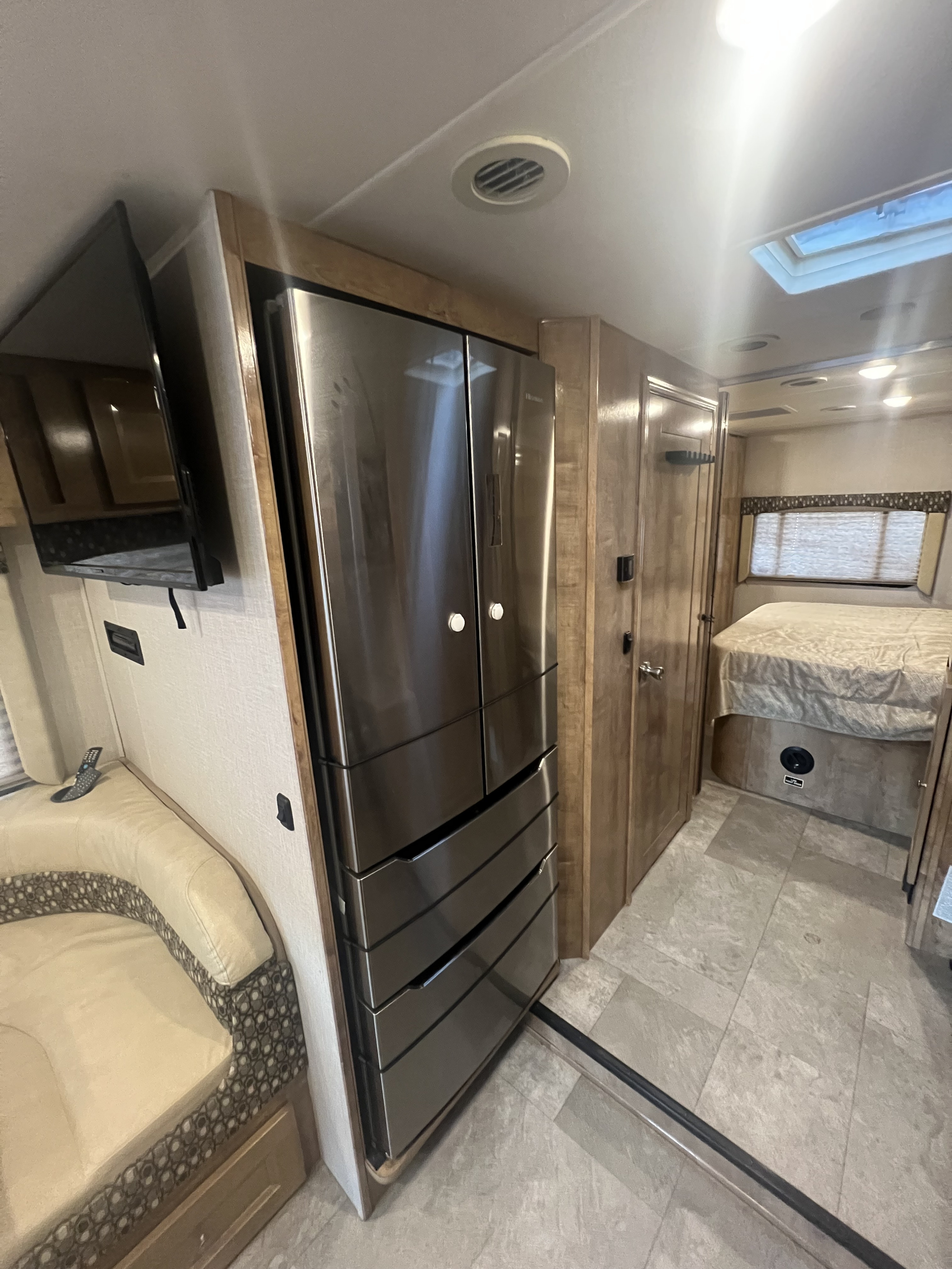 RV rental interior featuring a modern stainless steel fridge, wall-mounted TV, U-shaped dinette, and a bedroom area.. Forest River Coachmen Leprechaun 2020