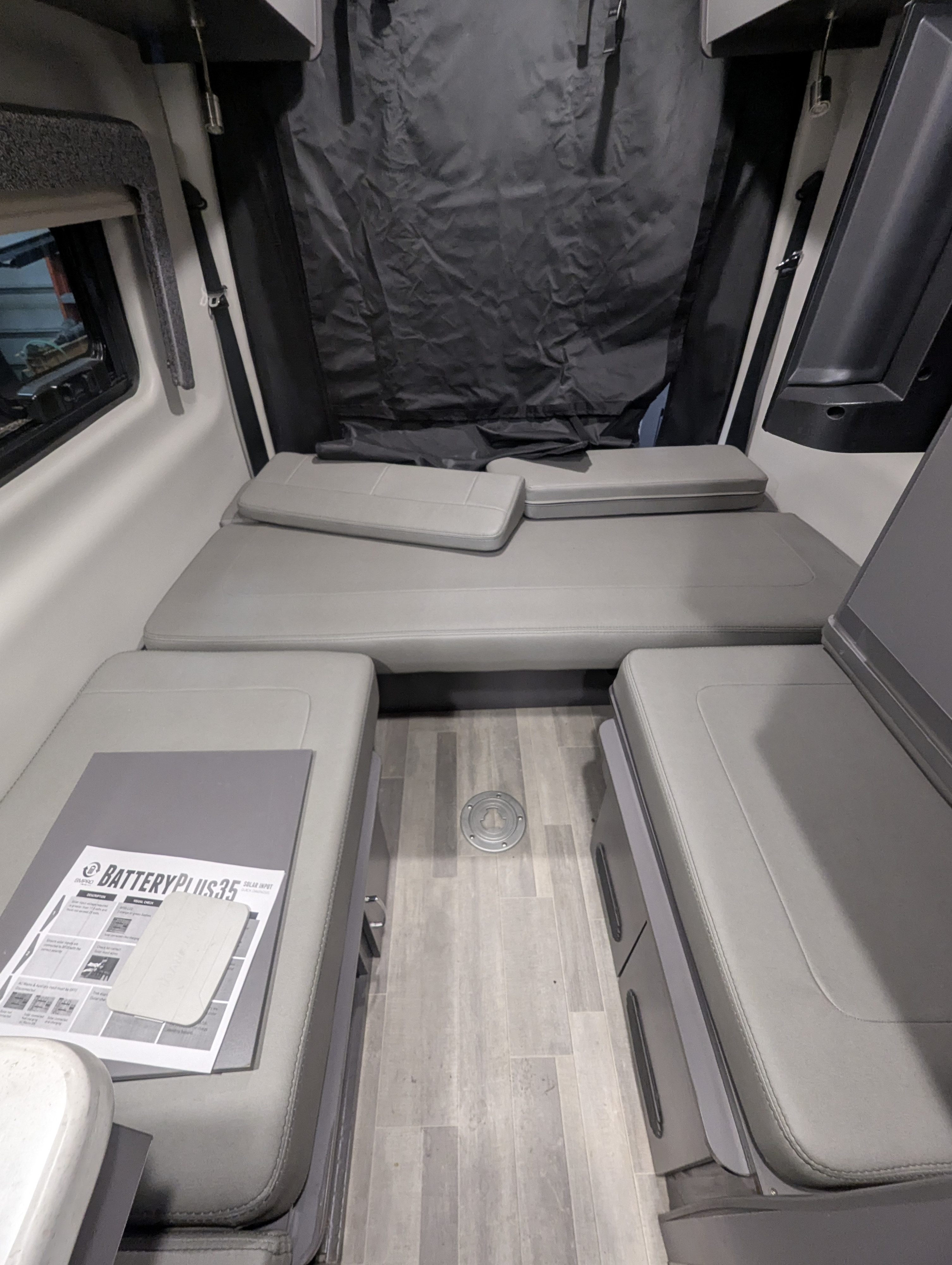RV rental camper van interior: Compact sleeping/seating area with grey cushions and wood-look floor.. Thor Tranquility 2023