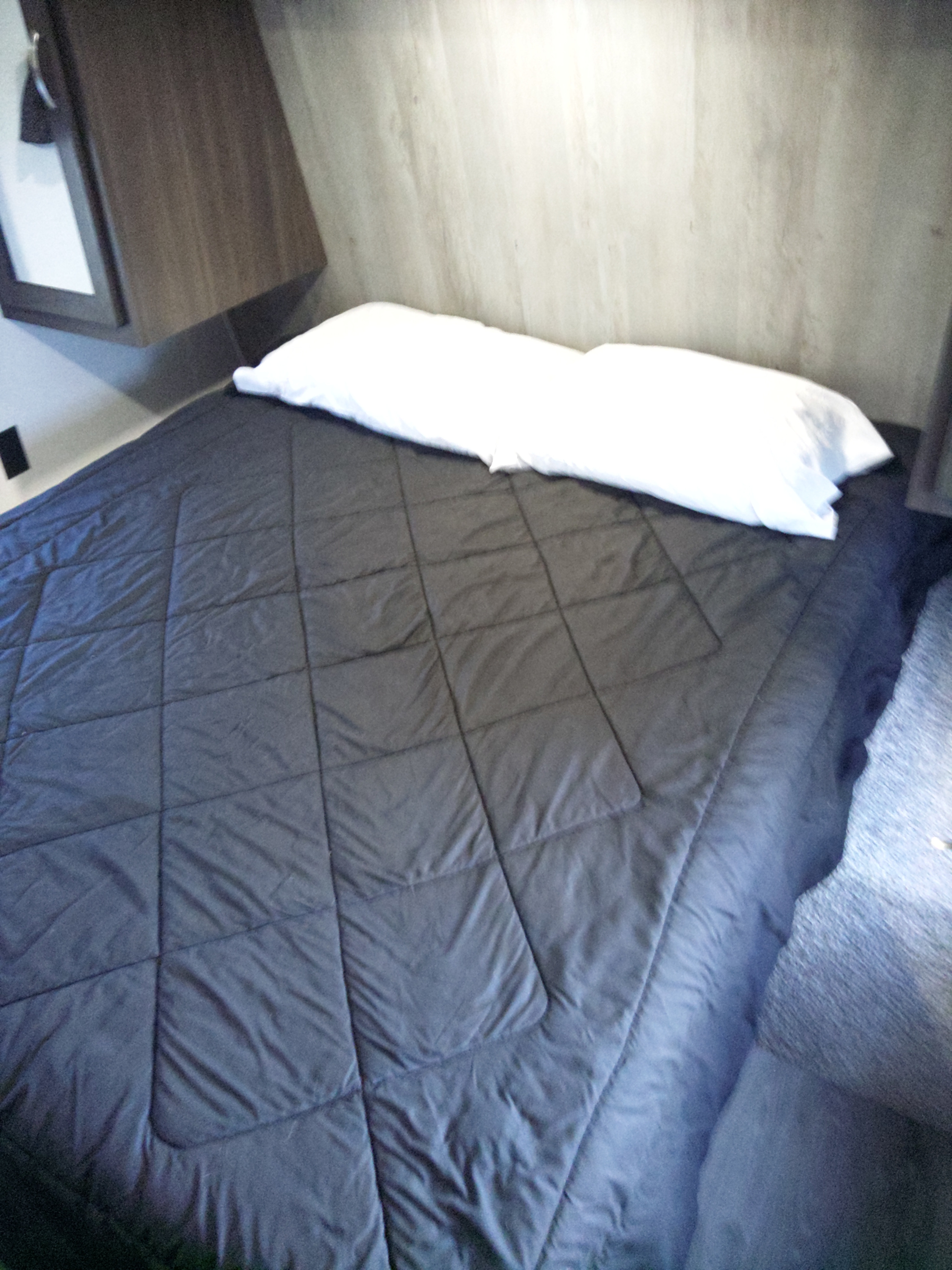 RV rental: Cozy sleeping area featuring a dark quilted comforter and white pillows, beneath a wood cabinet.. Keystone RV Springdale 2020