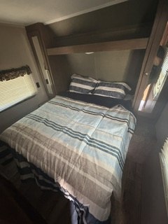 Cozy RV rental bedroom with a comfortable double bed, striped bedding, overhead storage, and small windows, ideal for travel.. Keystone RV Hideout LHS 2018