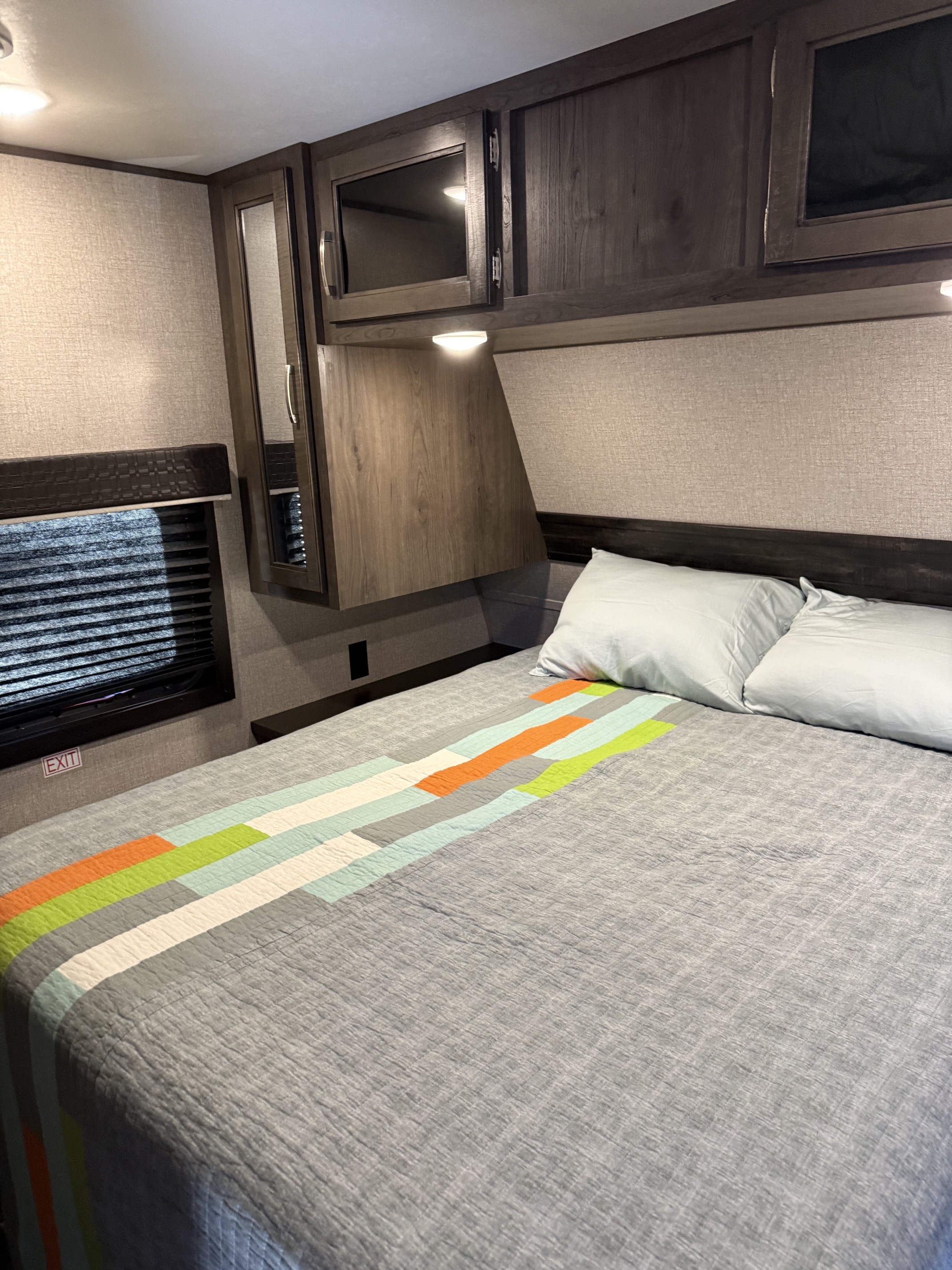 Cozy RV rental bedroom features a bed with a colorful striped quilt, overhead storage, textured walls, and soft lighting.. Jayco Jay Flight 2021