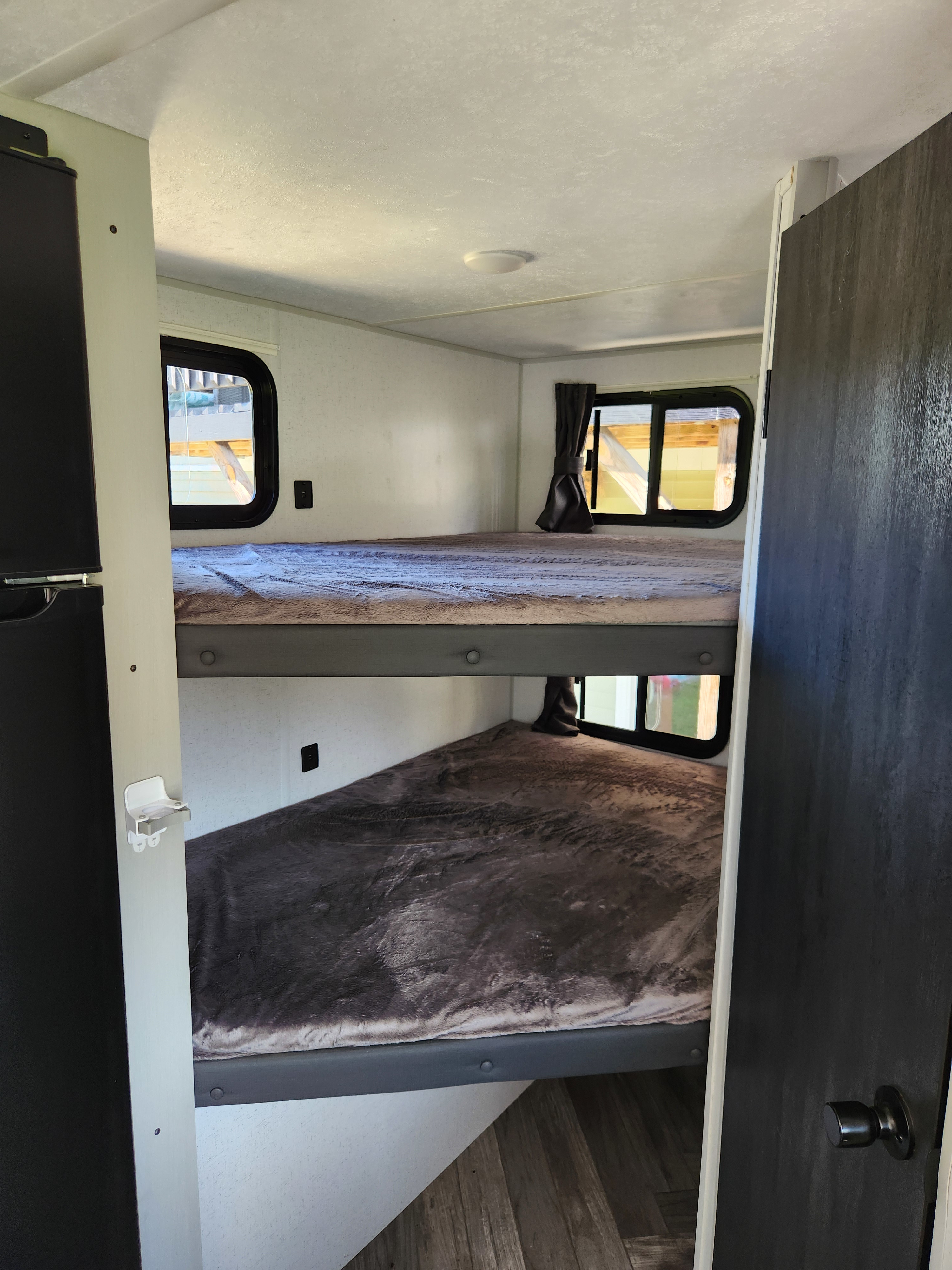 View of an RV rental's interior with stacked bunk beds, each featuring a window and cozy blanket. Great sleeping space.. Forest River Wildwood FSX Plantium 2022