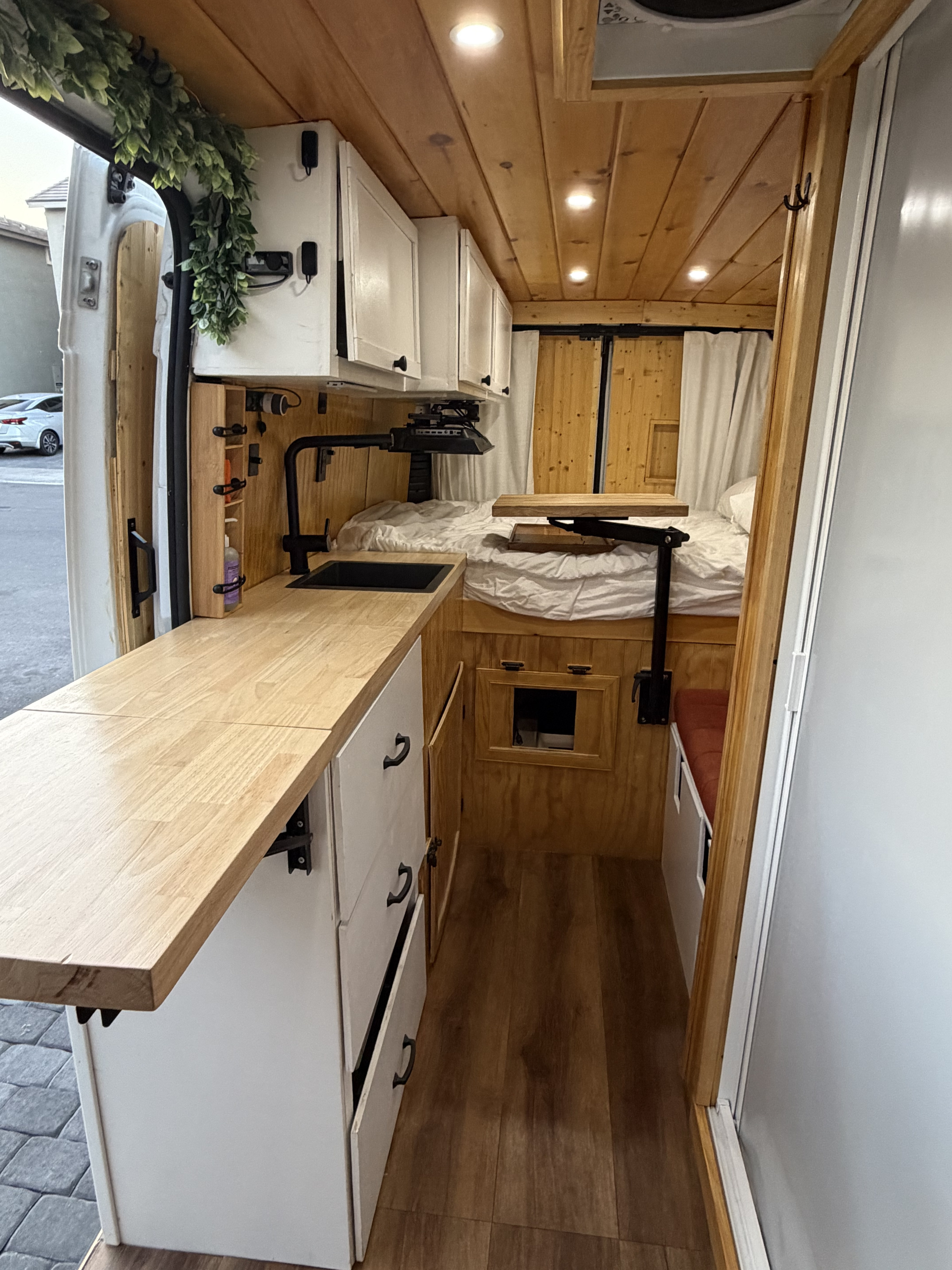 Inside an RV rental: a cozy van interior with a wood-paneled kitchen, bed, and efficient storage for compact living.. Dodge Ram 2500 2024