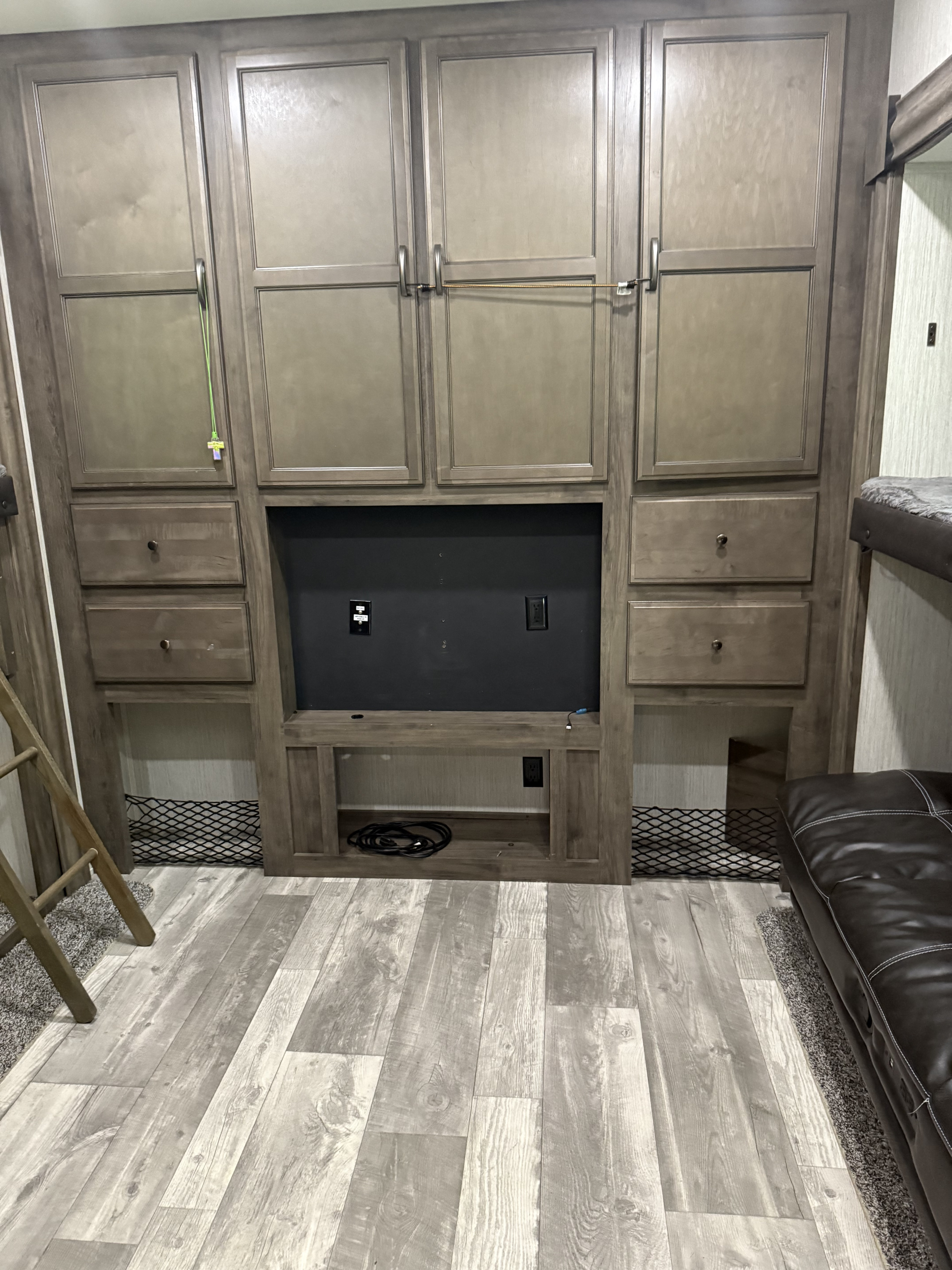 RV rental interior: built-in storage, TV mount, cabinets, drawers. Bunk ladder, sofa, and light wood-look floor are also visible.. Forest River Sandpiper 2021