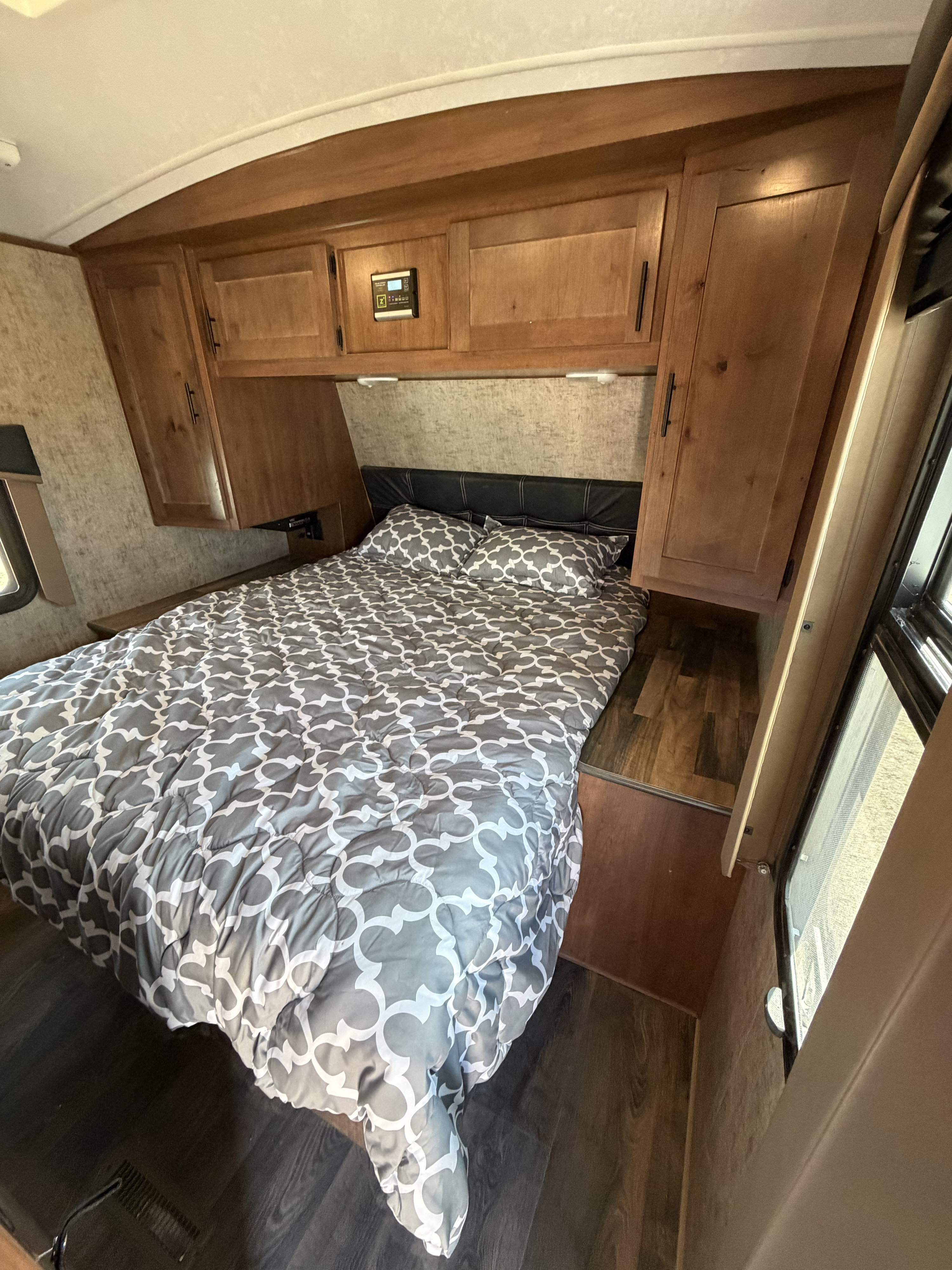 Cozy RV rental bedroom with a bed featuring a gray and white geometric comforter, overhead wooden cabinets, and a window.. Outdoors RV Mountain Trax Backcountry 2022