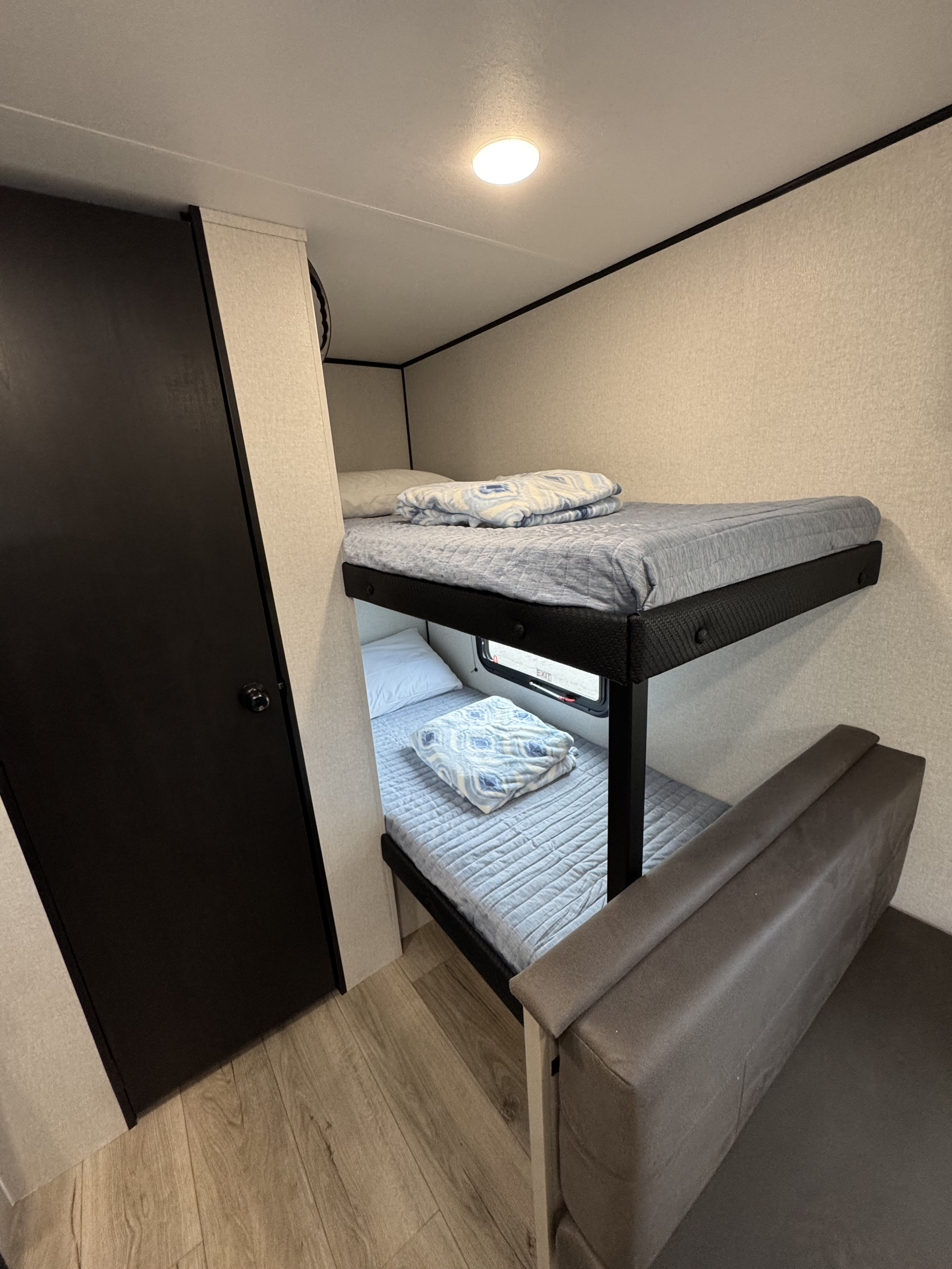 Inside an rv rental: cozy bunk beds with light blue bedding, a dark door, and wood-look flooring. Ready for adventures.. Jayco 17HB 2026