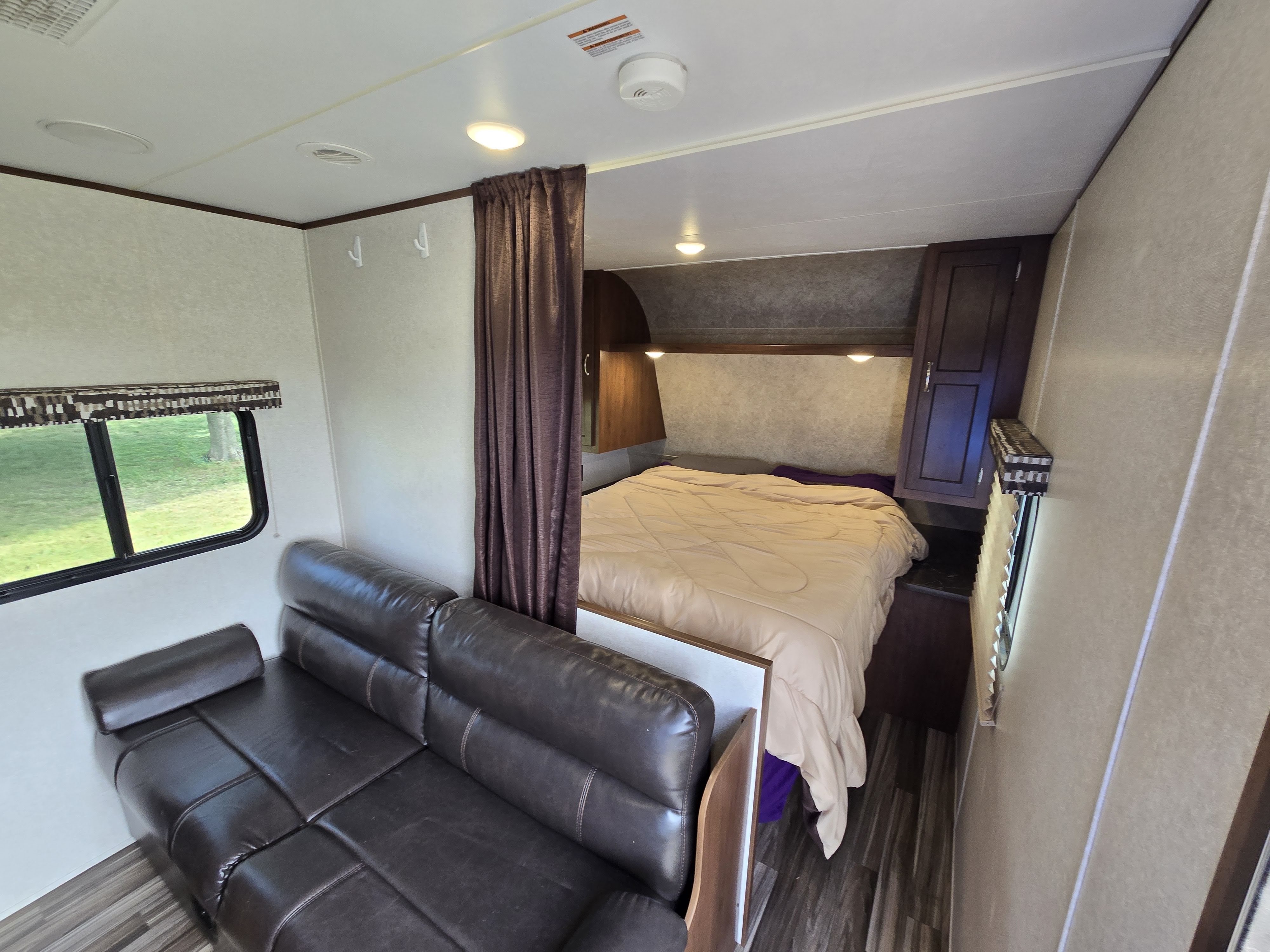 RV rental interior: Cozy bedroom with bed and privacy curtain, next to a comfy brown leather couch and window in the living area.. Jayco Jay Flight SLX 2017