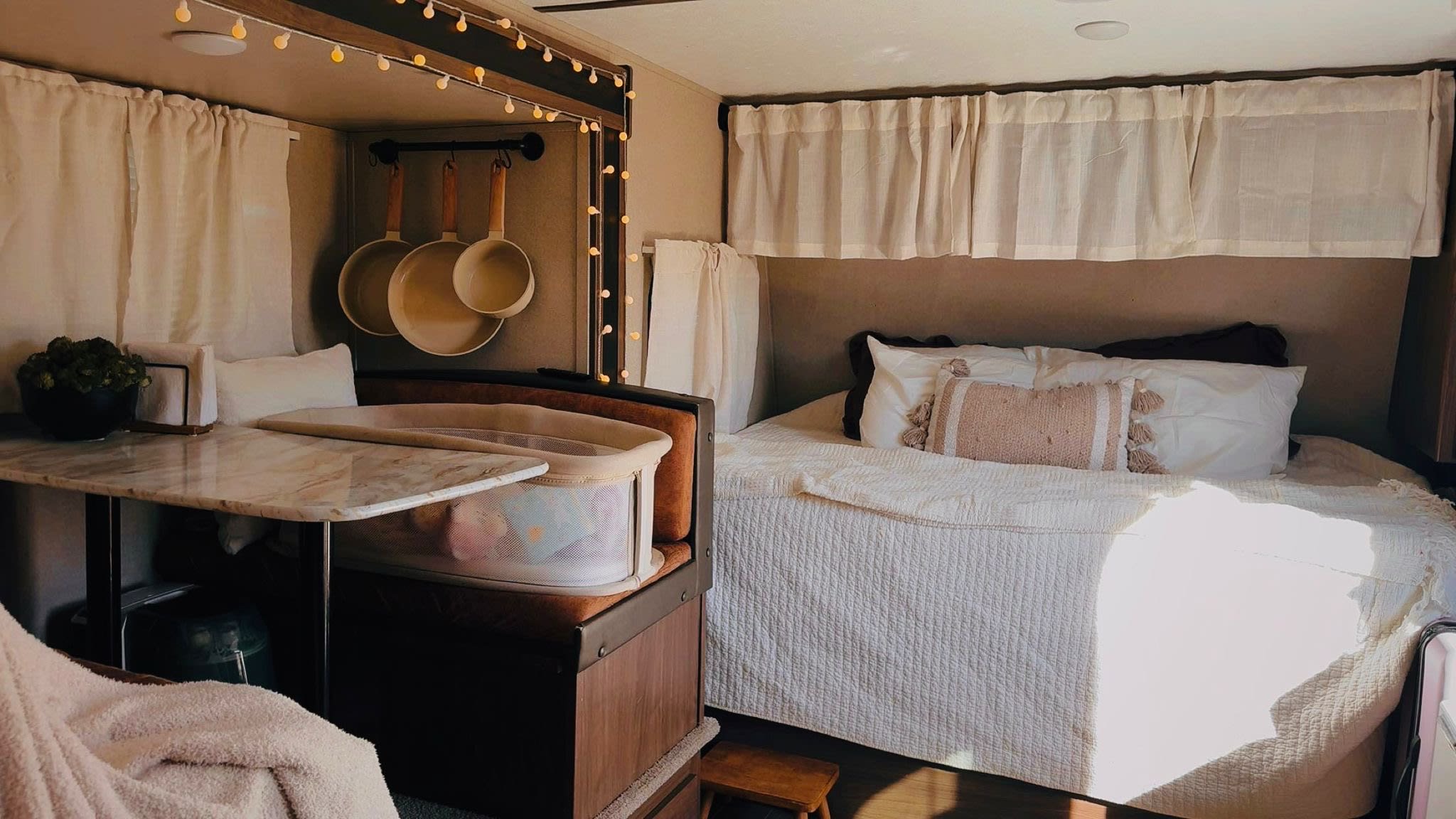 A cozy RV rental interior showcases a bed, dining space with a baby bassinet, and hanging pots. Ideal for comfortable family travel.. Keystone RV Hideout LHS Mini 2019
