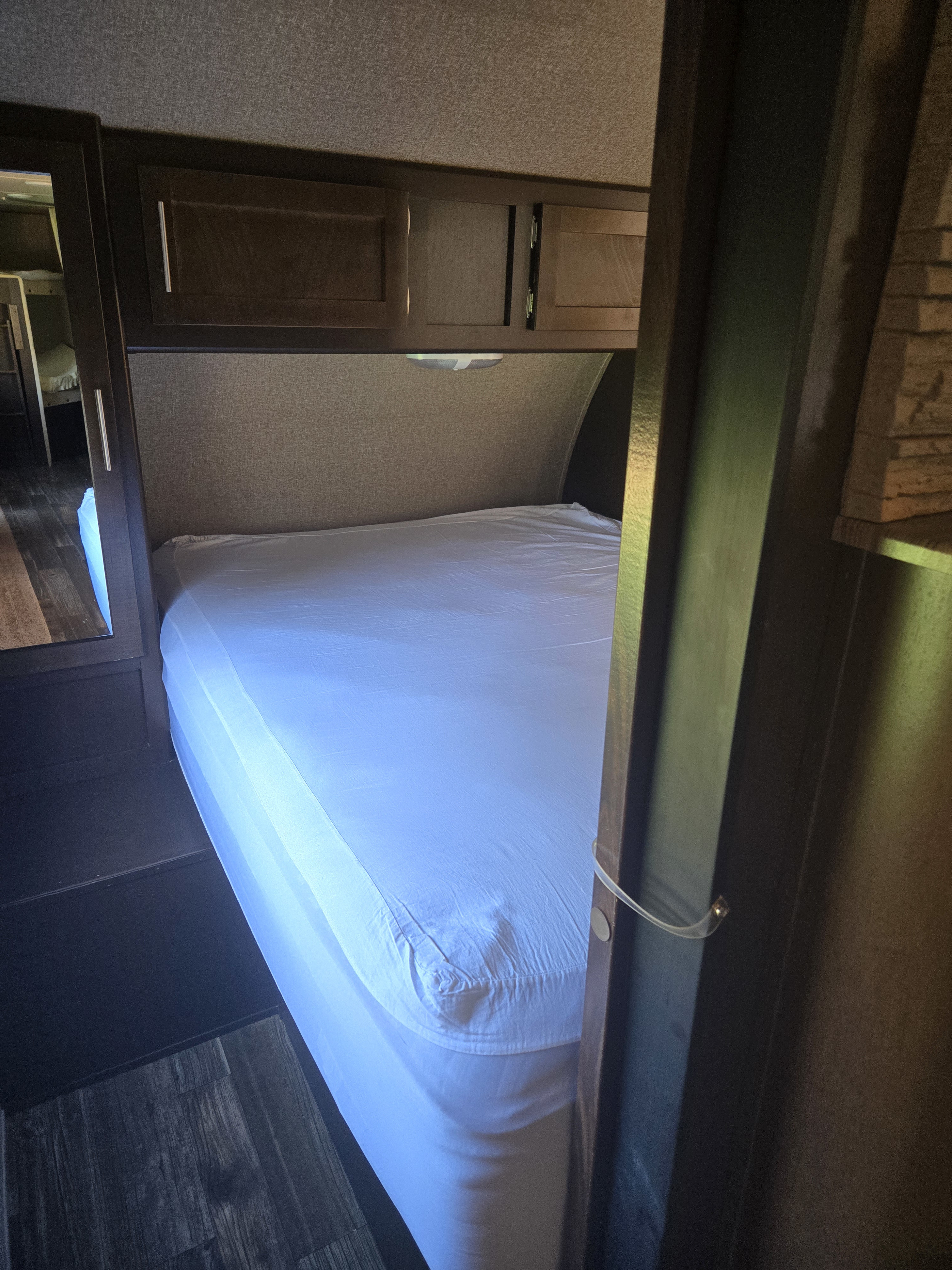 Cozy rv rental bedroom features a neatly made bed with white sheets, dark wood overhead cabinets, and a mirrored closet door.. Forest River Cherokee 2016