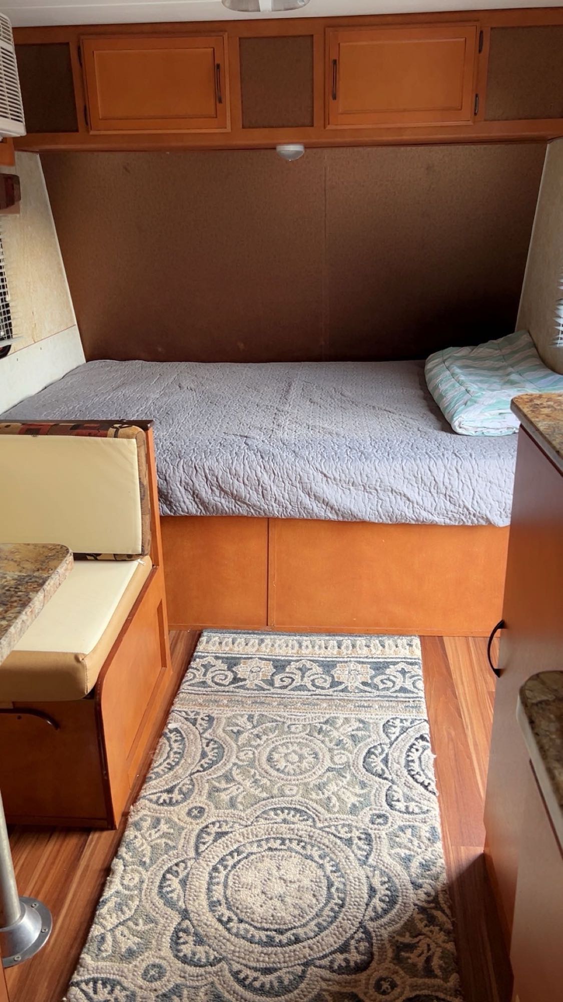 Inviting RV rental interior features a bed, dinette, and overhead cabinets with warm wooden tones and a decorative rug.. Gulf Stream Ameri-Lite 2018