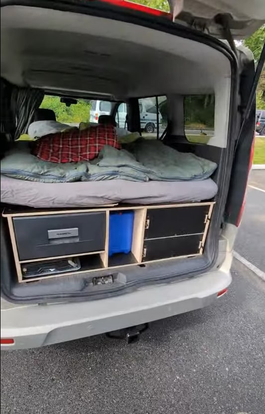 Inside an rv rental camper van: a bed over storage, with a portable fridge and drawers. Ready for travel and van life.. Ford Transit 2016
