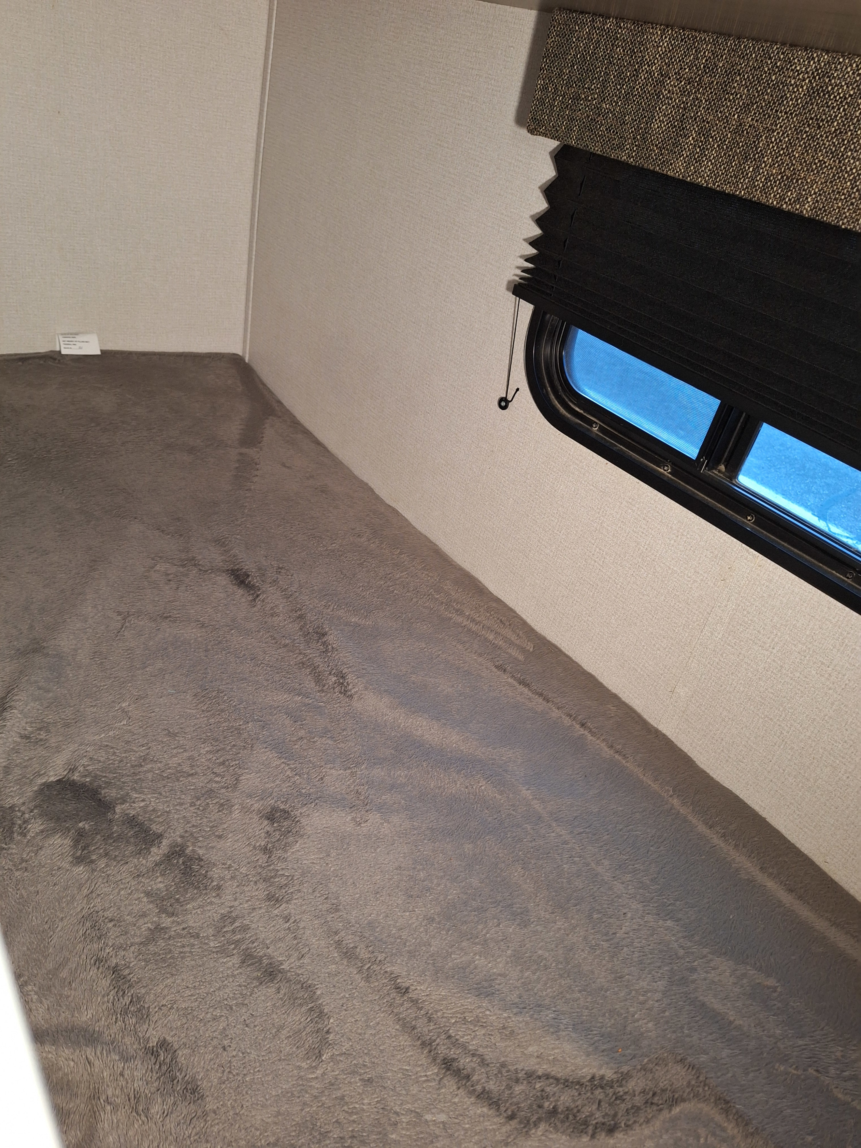 Cozy RV rental bunk bed with soft grey bedding, a textured wall, and a window with a black pleated blind.. Keystone RV Hideout LHS Mini 2020