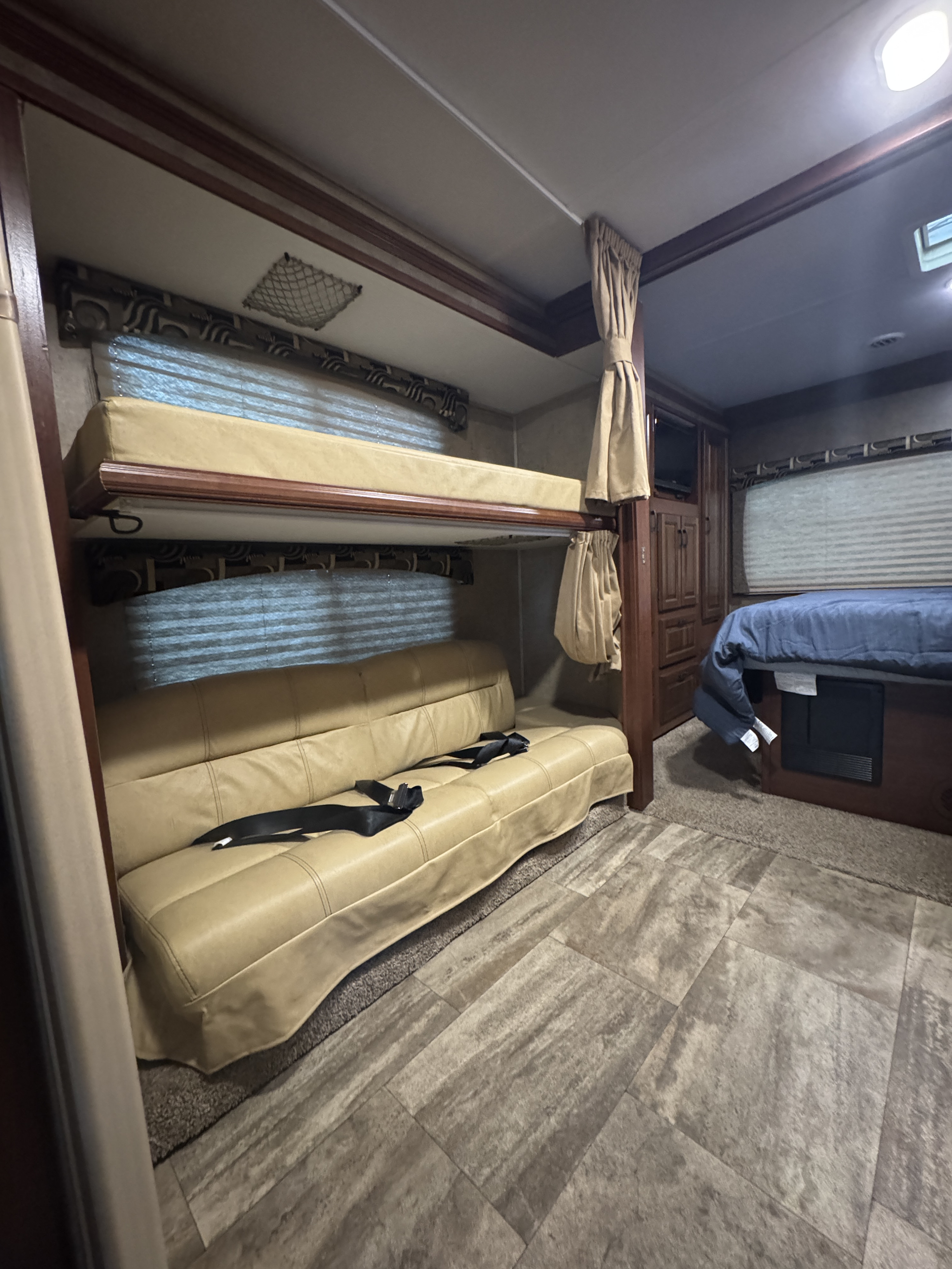 This RV rental interior features bunk beds, a sofa with seatbelts, and a main bed, providing a compact, functional living space.. Forest River Sunseeker 2016