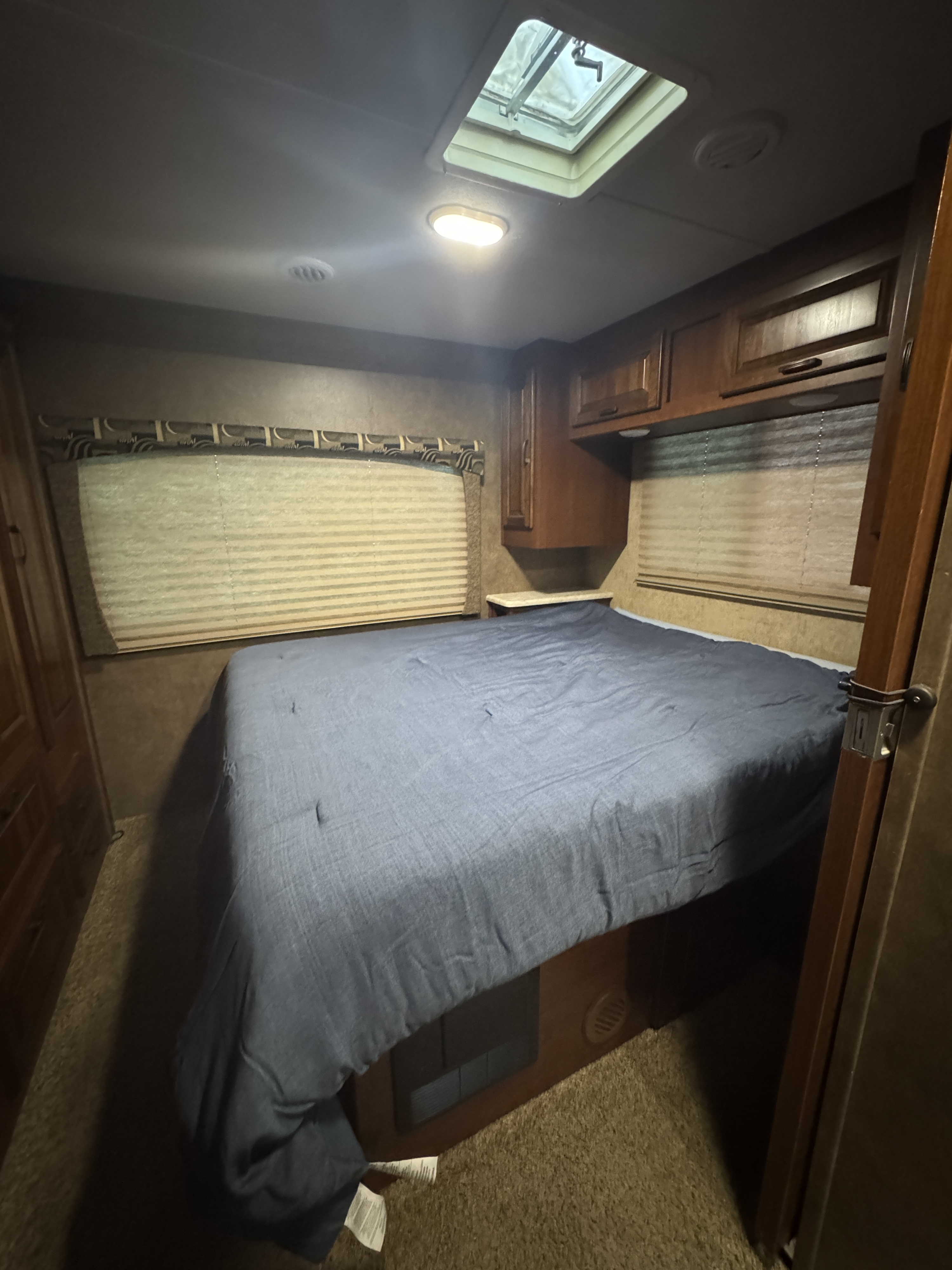 RV rental bedroom features a queen bed, wooden overhead cabinets, window blinds, and a ceiling skylight for light.. Forest River Sunseeker 2016