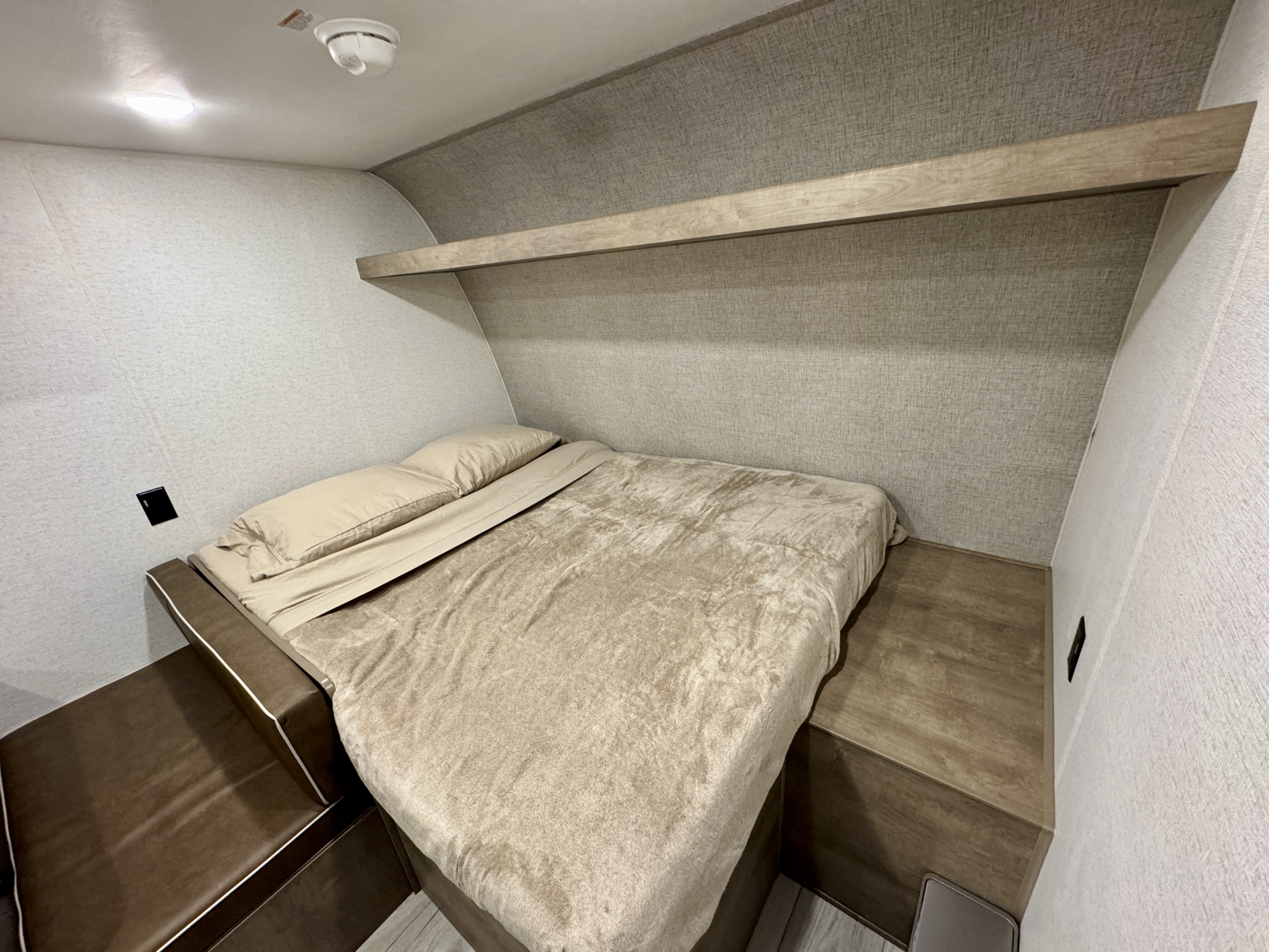 This cozy RV rental bedroom offers a comfortable bed, overhead shelf, and compact layout for your travel adventures.. Keystone RV Springdale Mini 2025