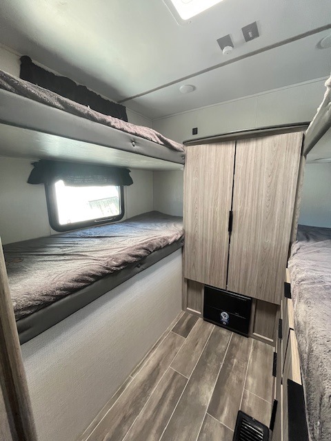 An rv rental bunkhouse shows two sets of bunk beds with a central cabinet, offering sleeping and storage space.. Keystone RV PP282QBWE22 2023