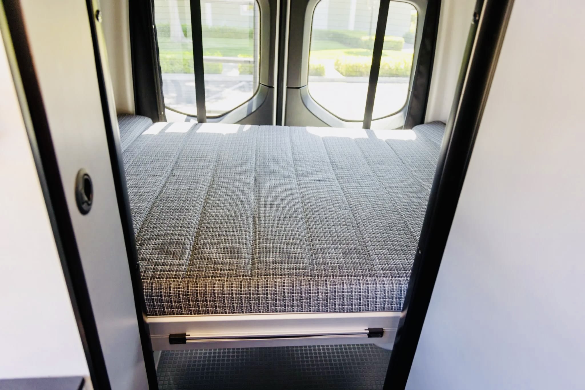 Inside this rv rental, a comfy campervan bed with a patterned mattress and rear windows, ready for your next adventure.. Winnebago Revel 2022