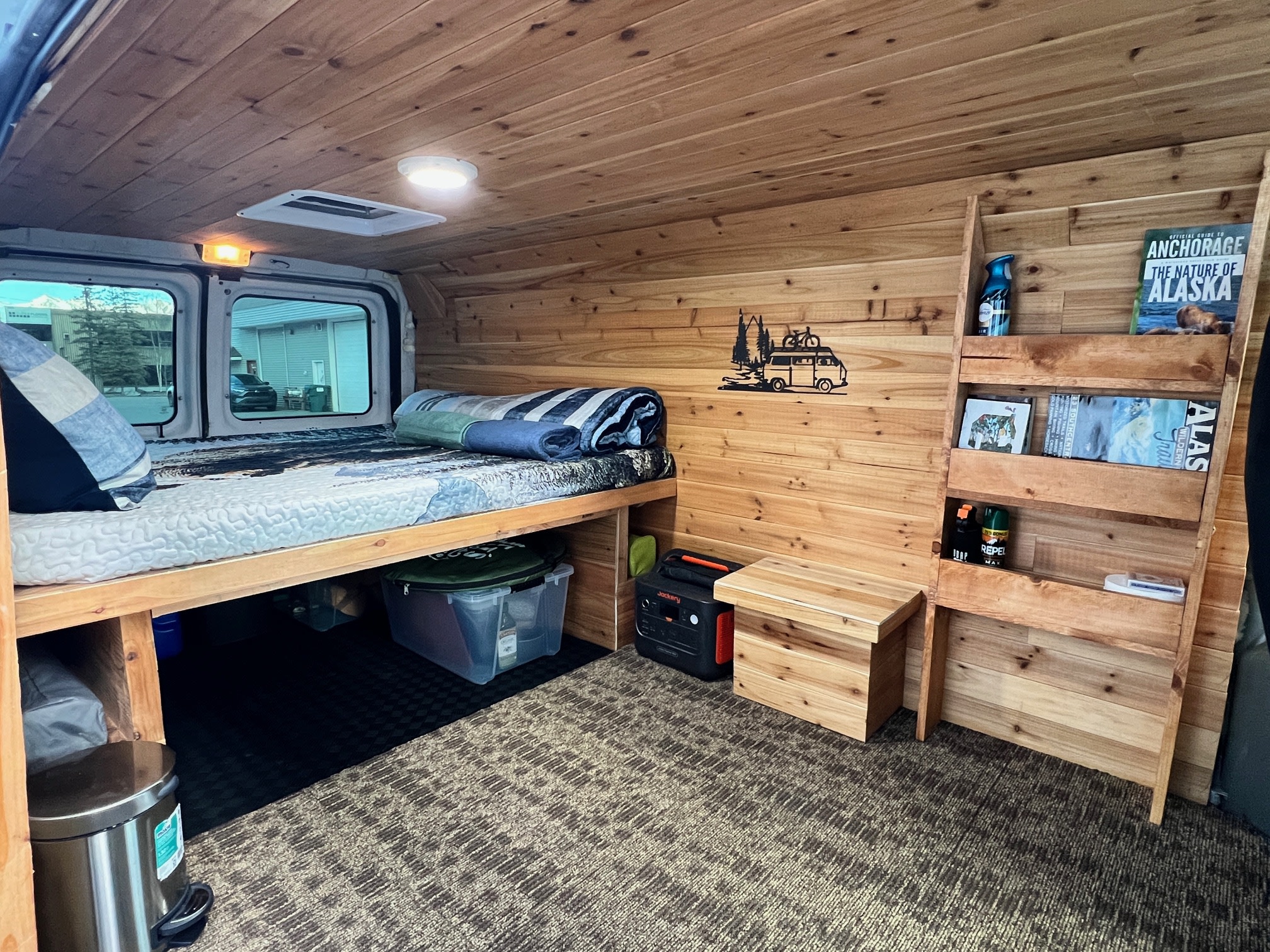 Cozy wood-paneled camper van interior with a bed, storage, and Jackery power station, ideal for an RV rental adventure.. Ford Econolline 250s 2013