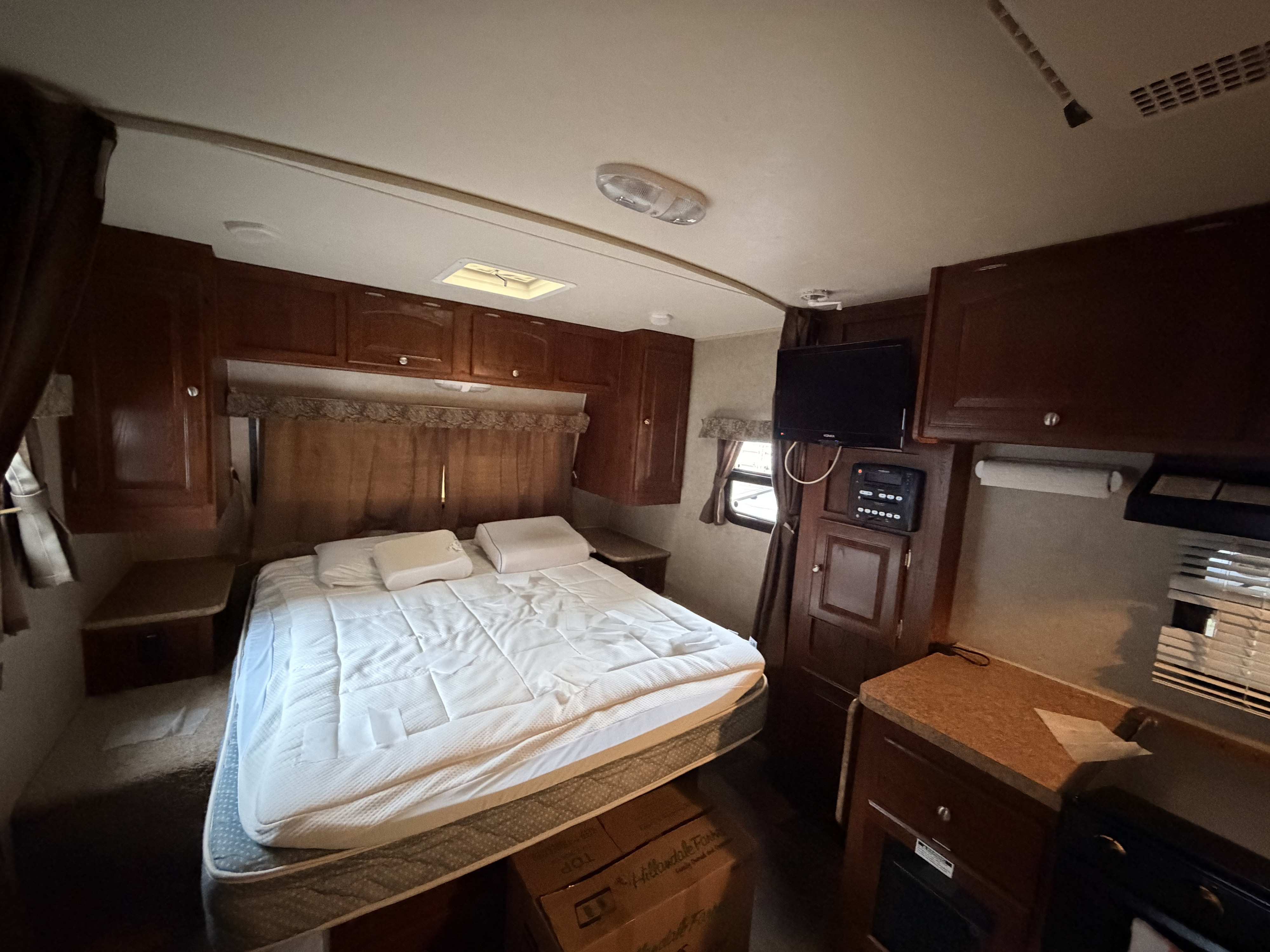 RV rental bedroom with ample overhead storage, TV, and an adjacent compact kitchen/galley area, offering a functional space.. Forest River Rockwood Mini Lite 2013