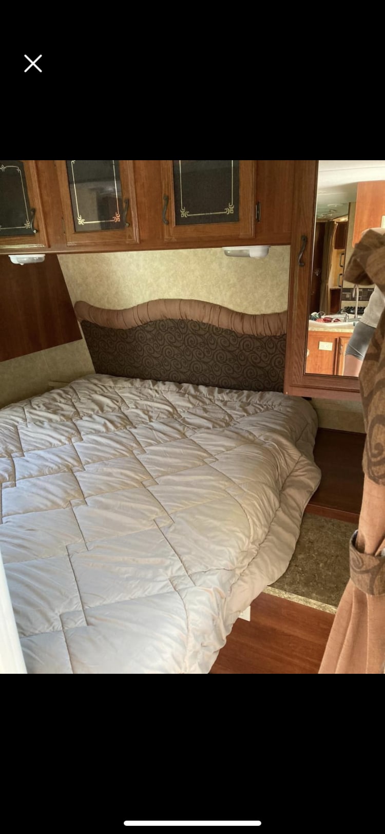 An inviting RV rental bedroom with a large bed, brown headboard, wood cabinets, and reflected kitchen view.. Forest River Tracer Executive 2010
