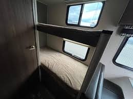 Inside an **RV rental**: a cozy bunk bed area featuring two single beds and windows, offering comfortable sleeping for guests.. Heartland RVs Pioneer 2018