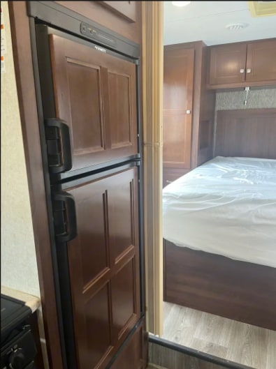RV rental: View of a wood-paneled Dometic refrigerator leading to a comfortable RV bedroom with a bed and built-in cabinets.. Forest River Sunseeker 2018