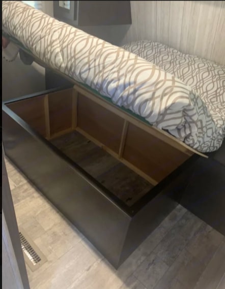 RV rental bed with mattress lifted, exposing a large under-bed storage compartment. Features patterned bedding & dark frame.. Heartland RVs Pioneer 2020