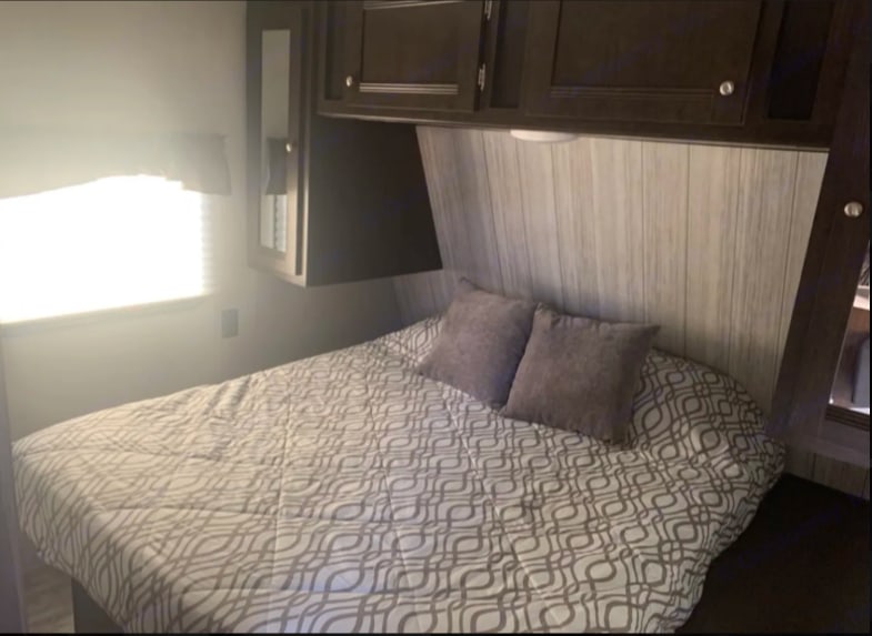 Comfortable RV rental bedroom featuring a queen bed with a patterned comforter, overhead cabinets, and a bright window.. Heartland RVs Pioneer 2020