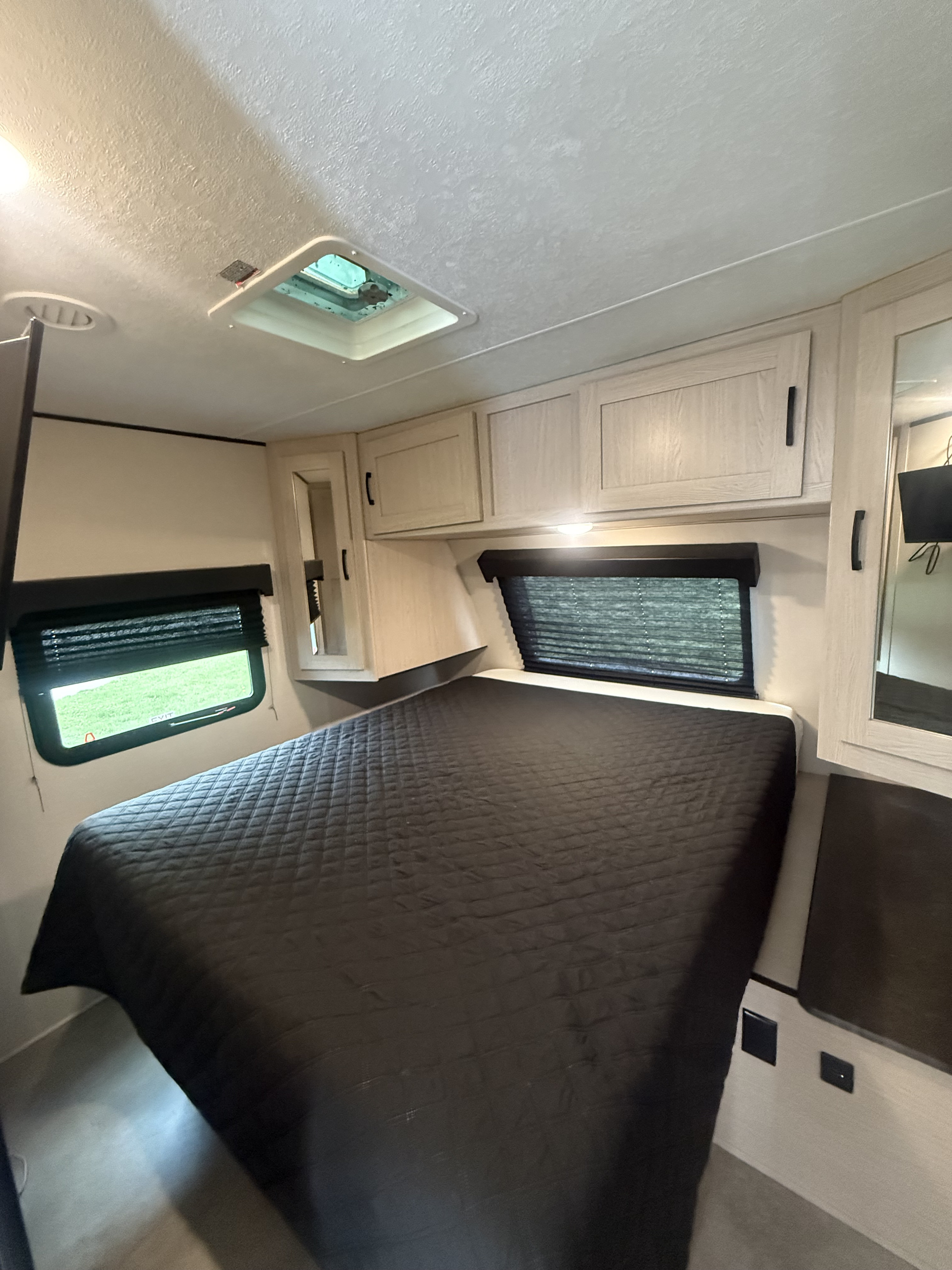 Comfortable RV rental bedroom featuring a large bed, overhead cabinets, windows with blinds, and a ceiling vent.. Coachmen Apex 2021