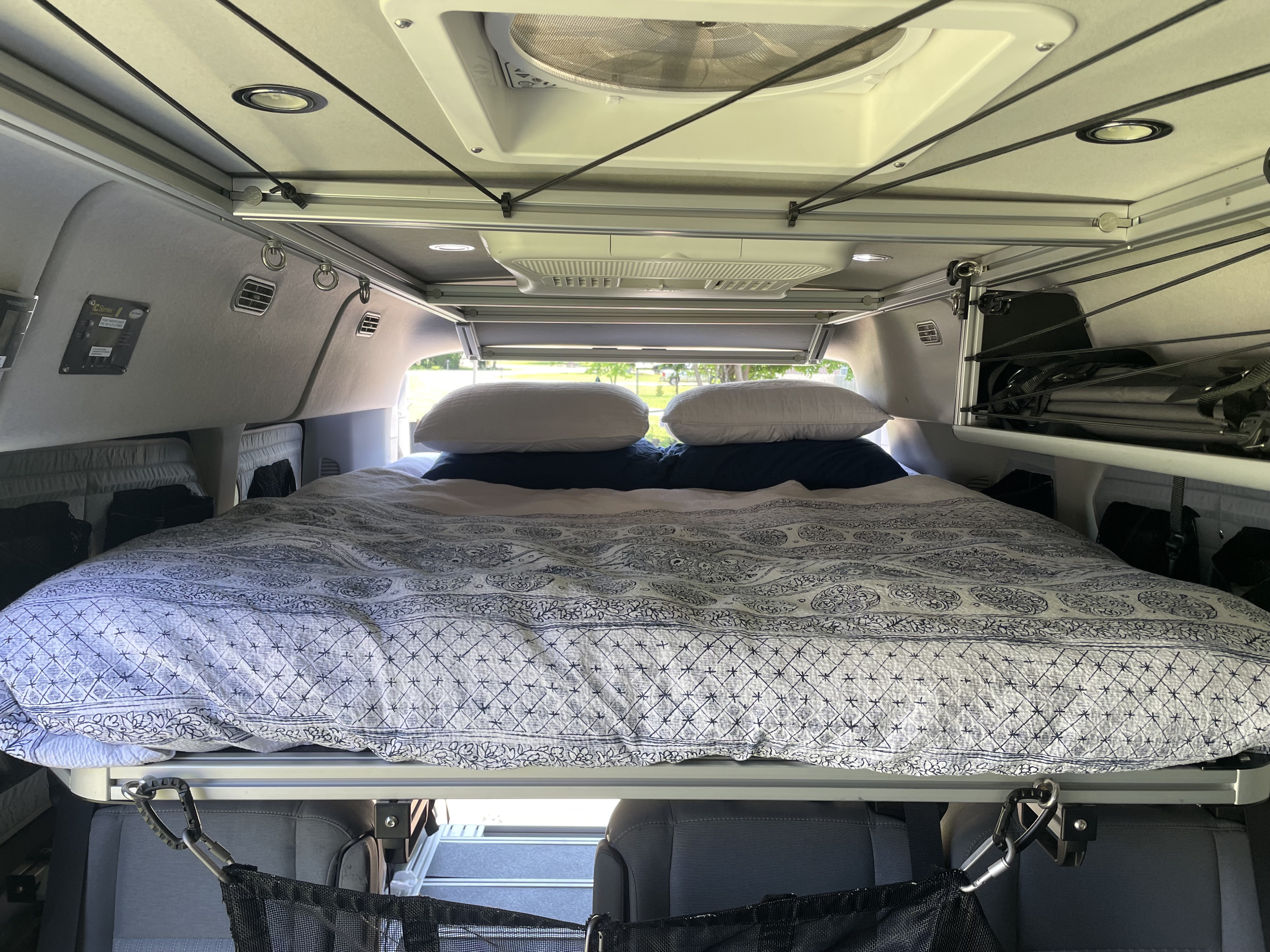 Inside an RV rental: a cozy bed with patterned bedding, overhead storage system, and fan for comfortable van life travel.. Ford Transit 2018