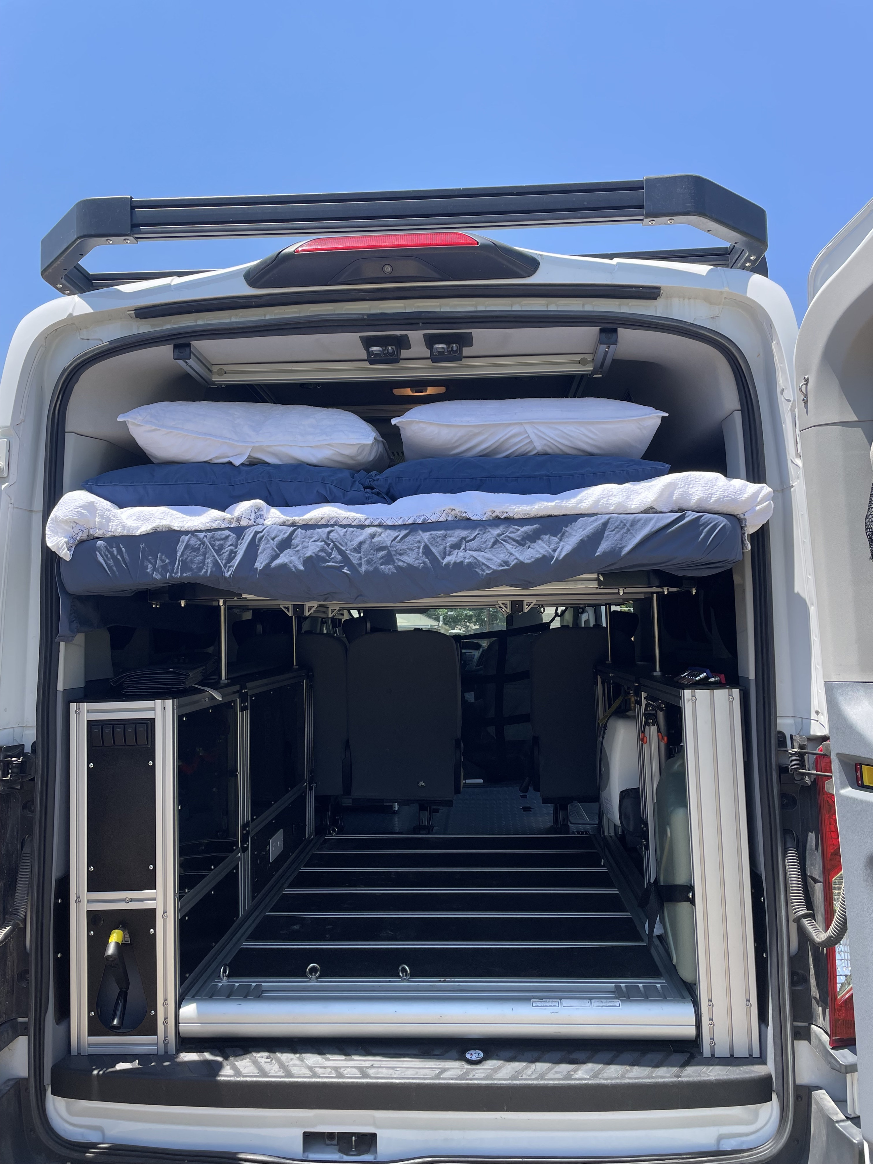 RV rental van conversion: Rear view shows a comfy raised bed, modular storage, and versatile interior layout.. Ford Transit 2018