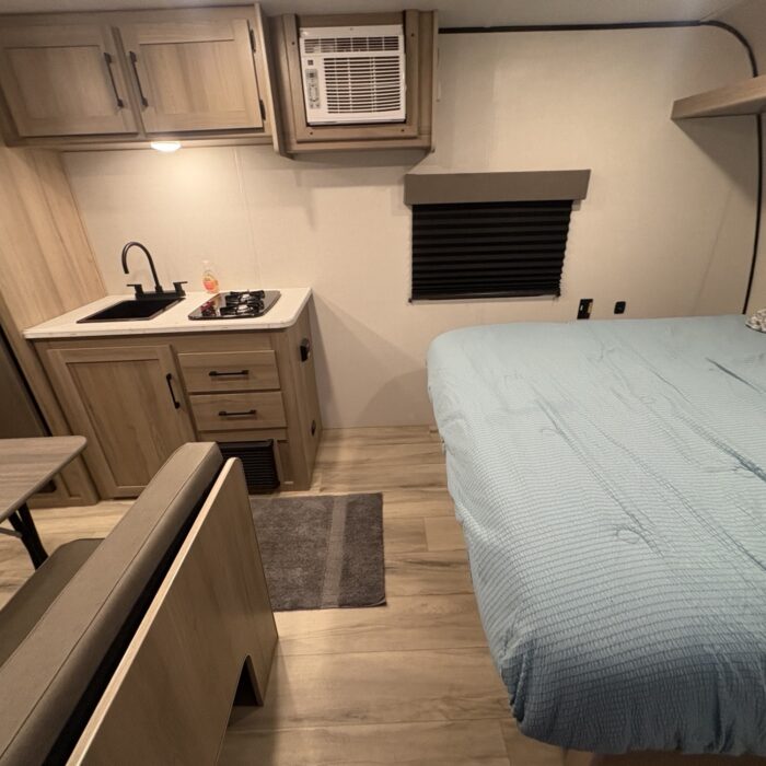 Cozy rv rental interior: features a compact kitchen (sink, stove), AC unit, comfortable bed, and dinette seating.. Keystone RV Coleman 2025