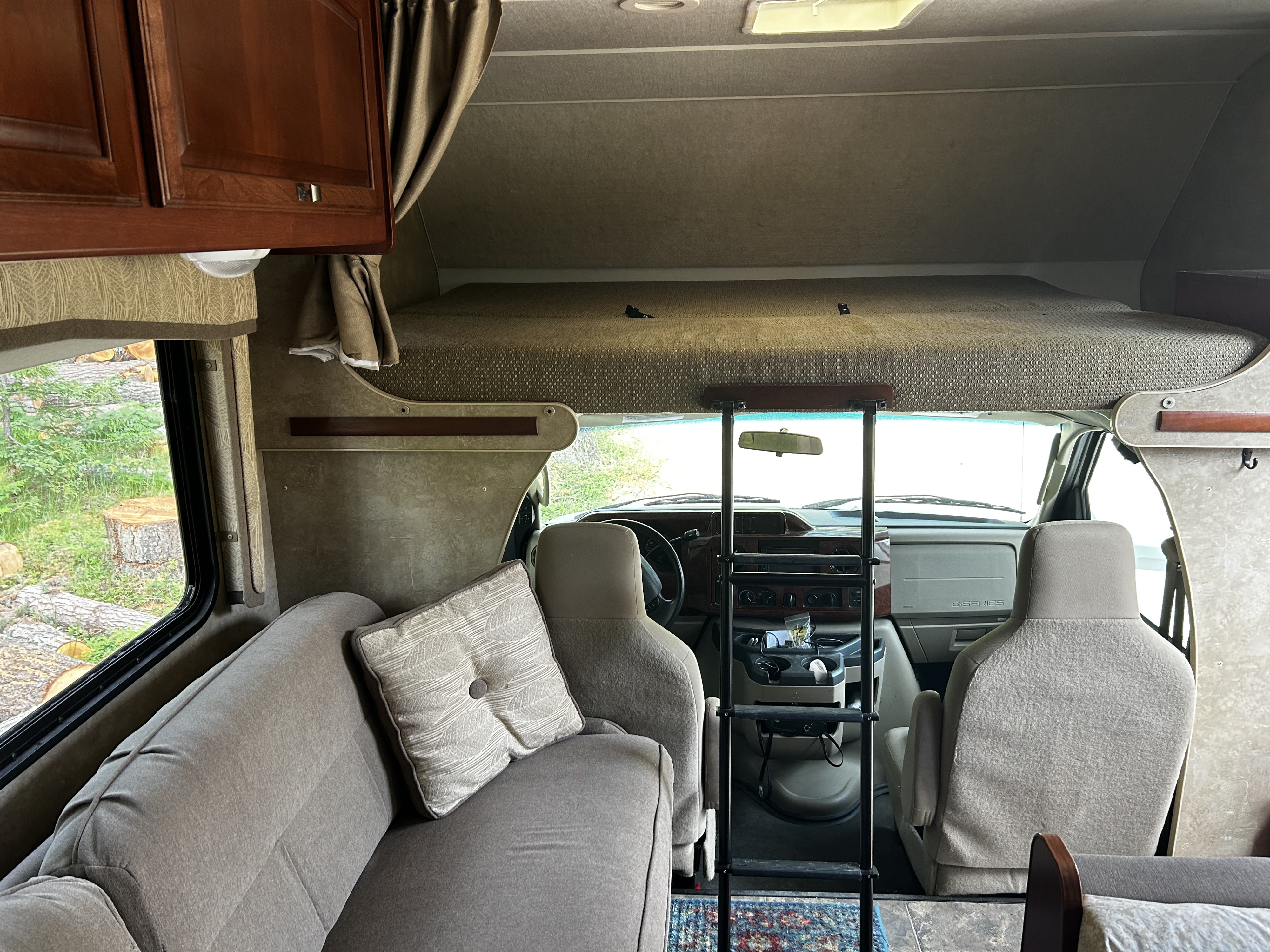 Interior view of an RV rental: a comfortable living area with a sofa, overhead bunk bed with ladder, and the driver's cab. Ideal for travel.. Winnebago Chalet 2014