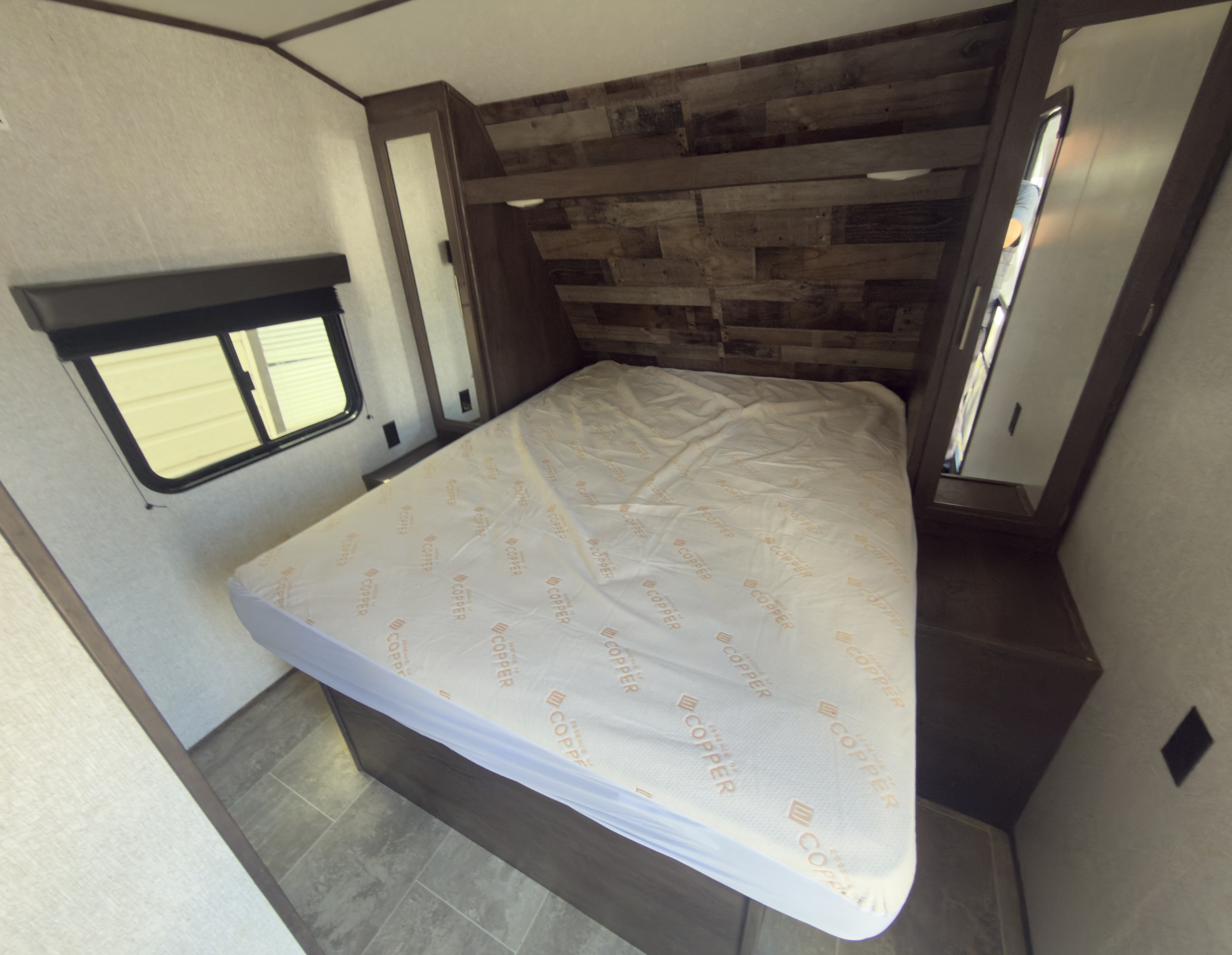 Explore this comfy RV rental bedroom featuring a large bed, window with blinds, and rustic wood-paneled walls. Ready for your travels!. Aspen Trail 2180RDWE 2020