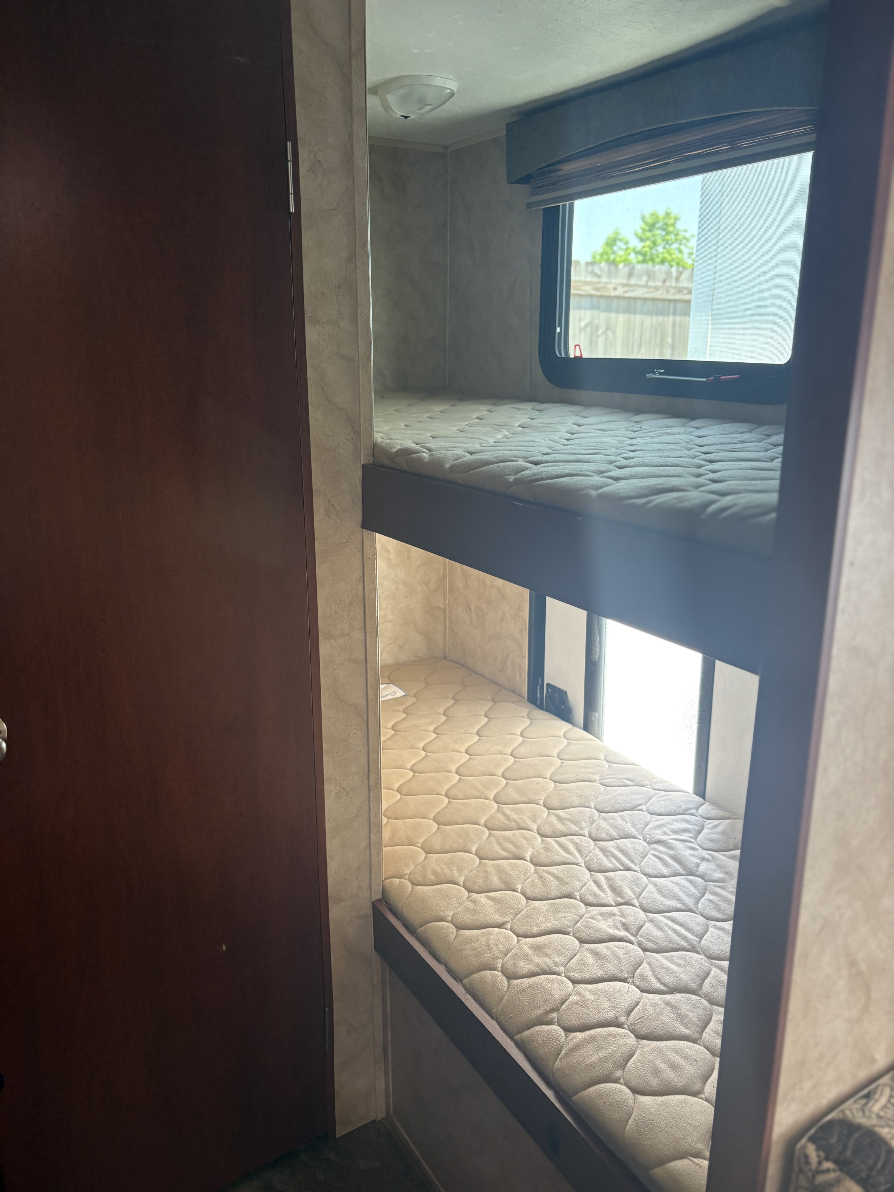 Cozy bunk beds inside this RV rental, with a window providing natural light and a nearby door, ready for your next adventure.. Coachmen Clipper 17BH 2015