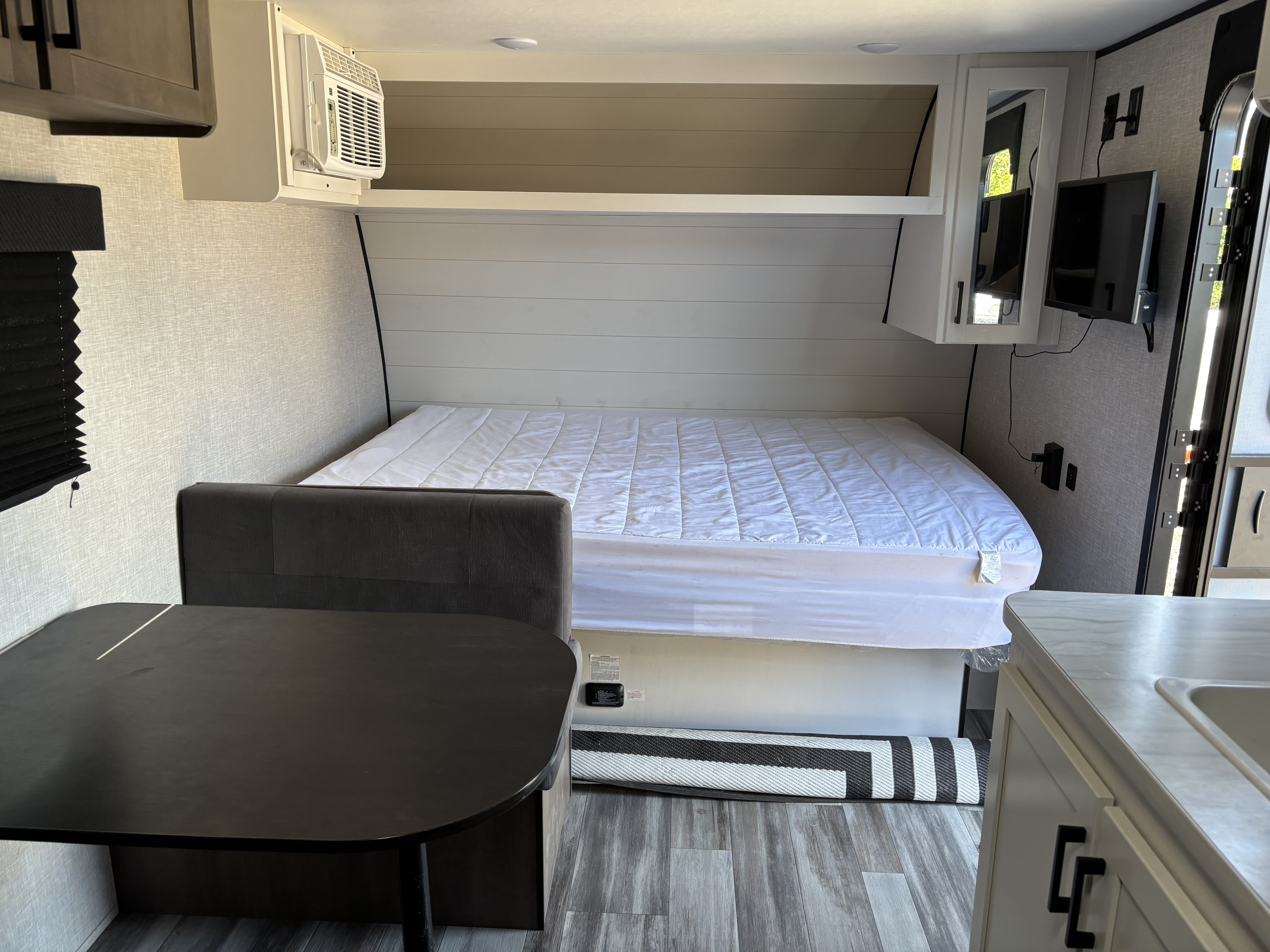Cozy rv rental interior featuring a neatly made bed, dining area, compact kitchen, and a small AC unit.. Jayco Jay Flight SLX 2025