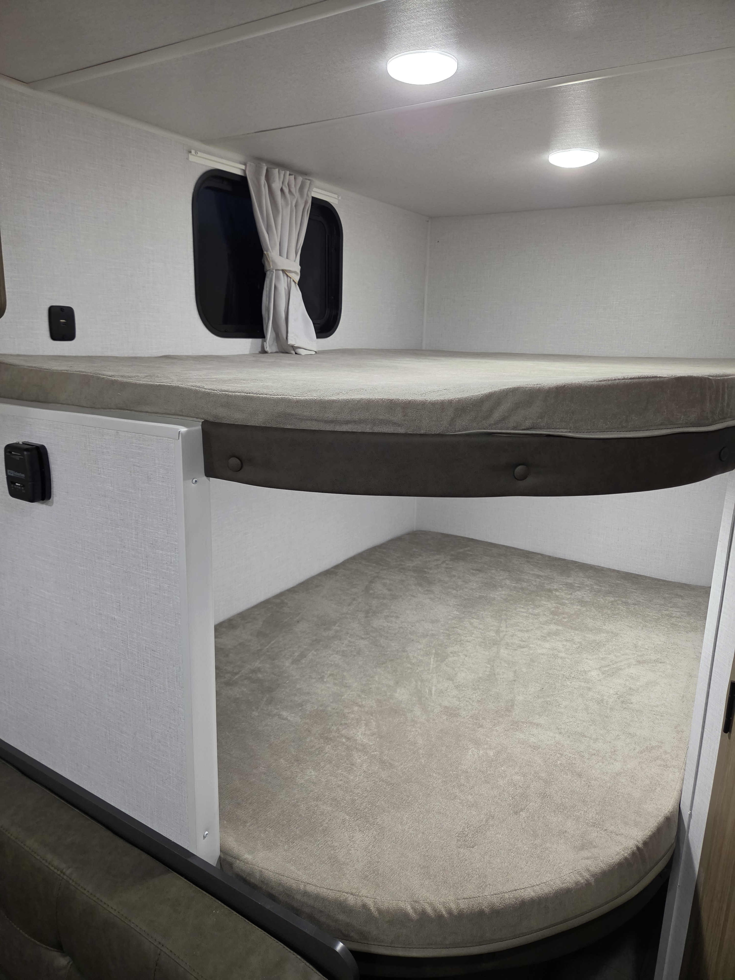 RV rental interior: light-colored bunk beds with mattresses, a window, and ceiling lights, creating a comfortable sleeping area.. Forest River Salem 2026