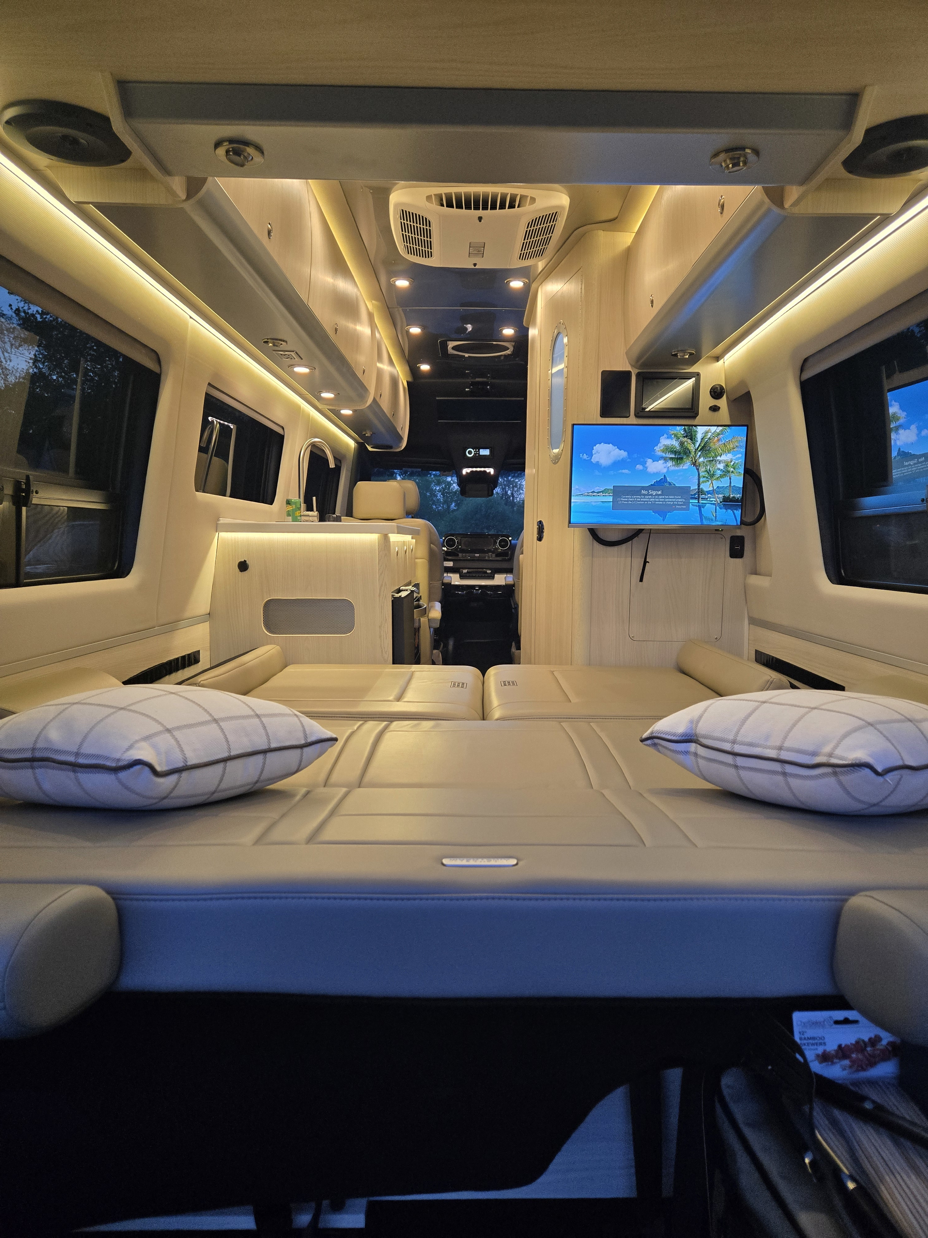 Spacious RV rental interior featuring comfortable beds, a kitchenette, and TV, warmly lit. Perfect for cozy road trips.. Airstream Interstate 2026
