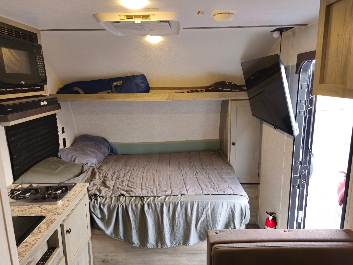 This RV rental interior features a cozy bed, kitchenette, TV, and an upper bunk, perfect for compact travel.. Sunset Park RV Sun Lite LTD 2026