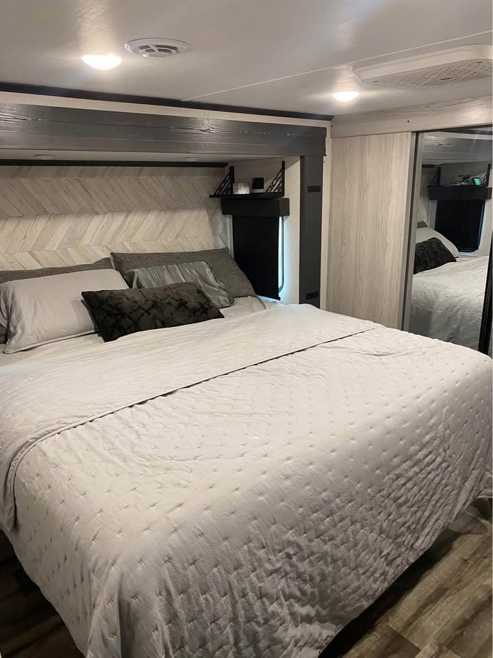Cozy modern RV rental bedroom featuring a chevron headboard, comfortable bed with light bedding, and mirrored closet.. Keystone RV Montana High Country 2024