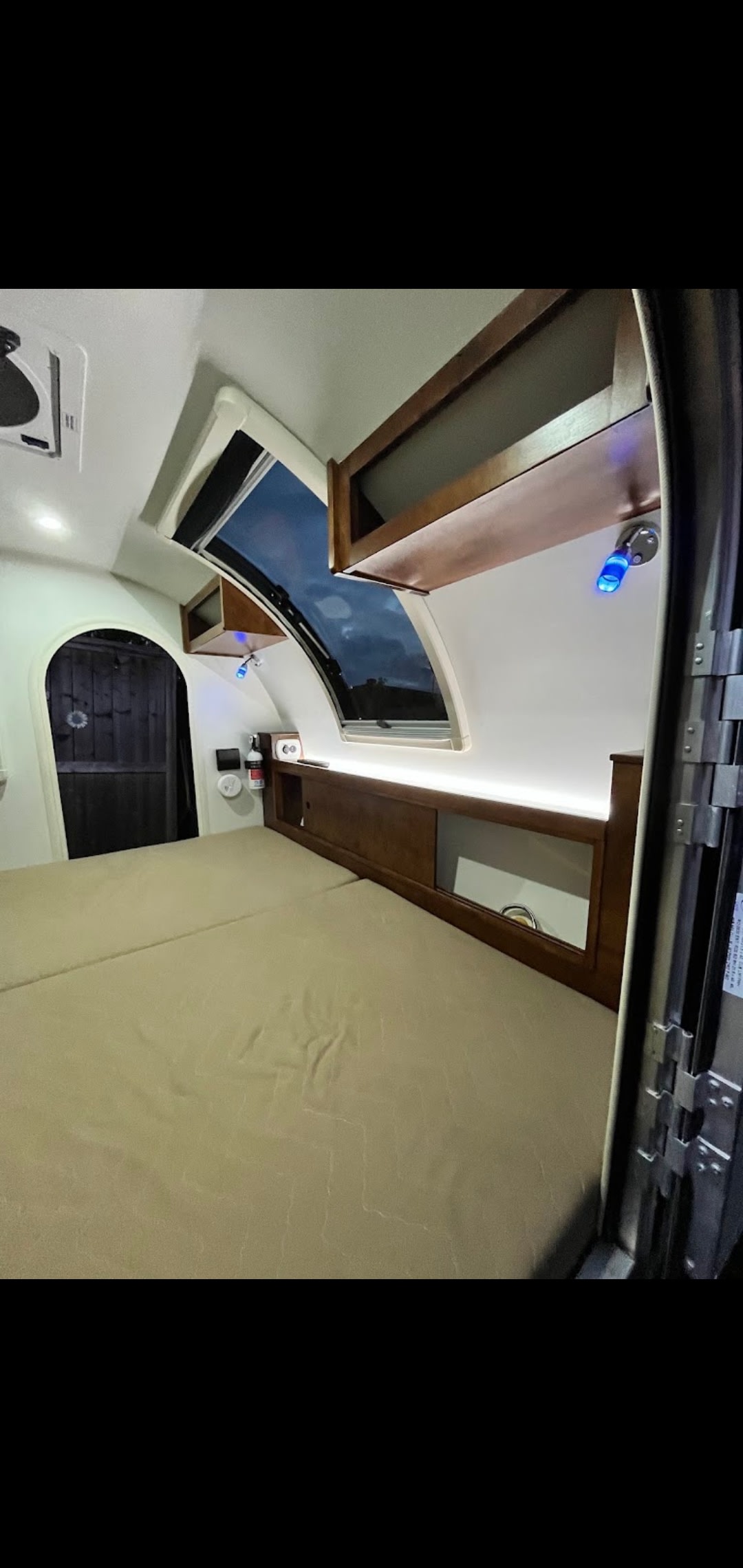 Cozy RV rental interior: bed, arched door, and curved skylight showing night sky. Warm wooden cabinets and lighting create comfort.. nuCamp T@G 2018