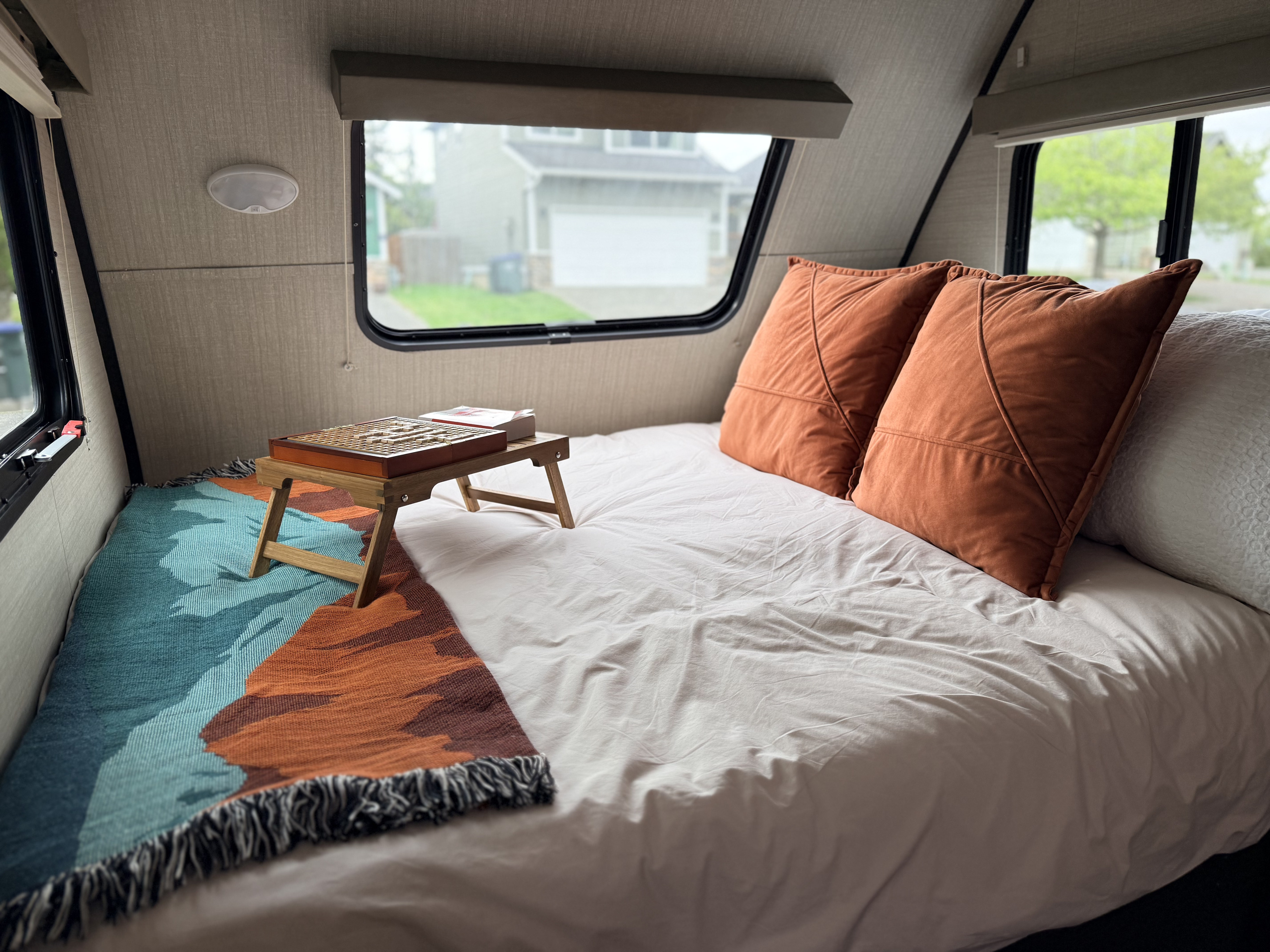 Cozy rv rental bedroom with a bed, pillows, colorful blanket, and a game on a tray, looking out to a neighborhood.. Keystone RV Bullet Colt 2018