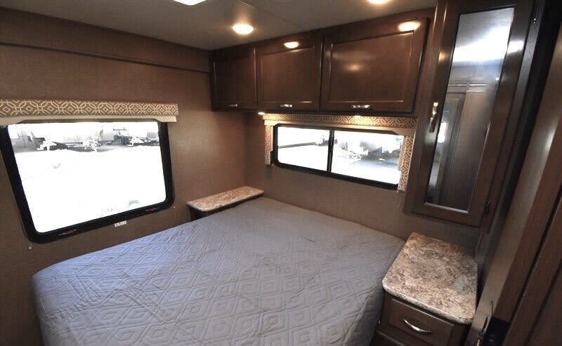 Cozy RV rental bedroom with a comfortable bed, overhead cabinets, and large windows for natural light.. Thor Freedom Elite 2017